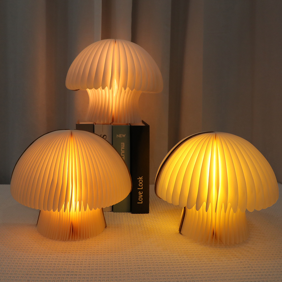 Drei beleuchtete Pilz-Lampen aus Papier auf einem Tisch mit Büchern im Hintergrund.