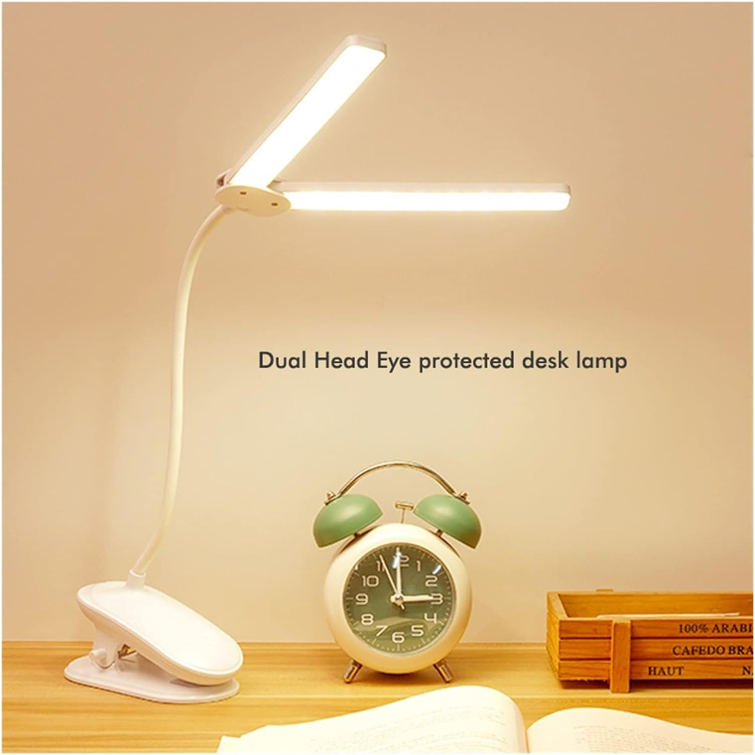 Weiße Schreibtischlampe mit zwei Leuchtköpfen und ein grüner Wecker auf Holz.