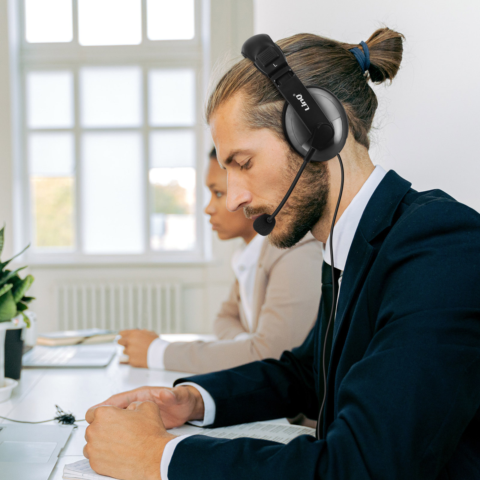 Un homme portant un casque, face à l'avant, avec une femme derrière lui. Ils sont dans un bureau.