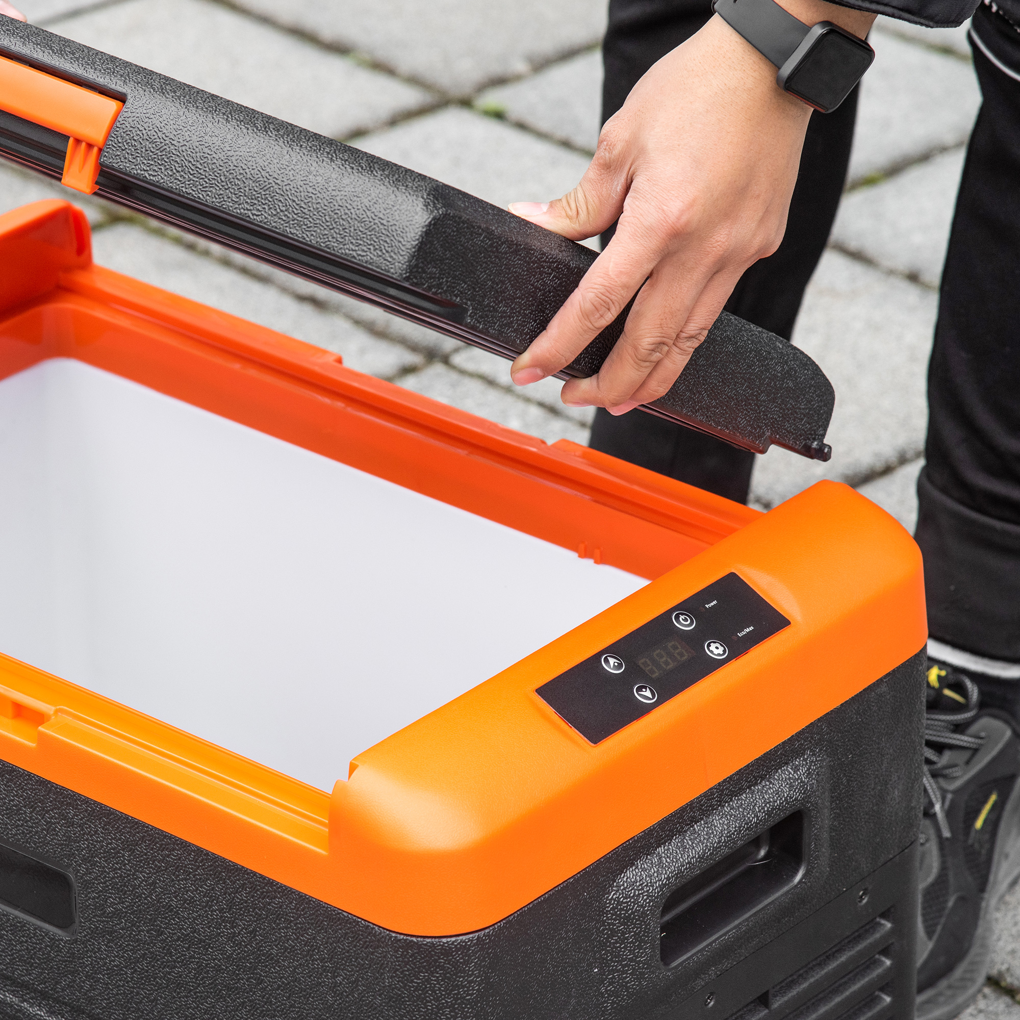 Una persona quita la tapa superior de una nevera negra y naranja. Visible un panel de control naranja.