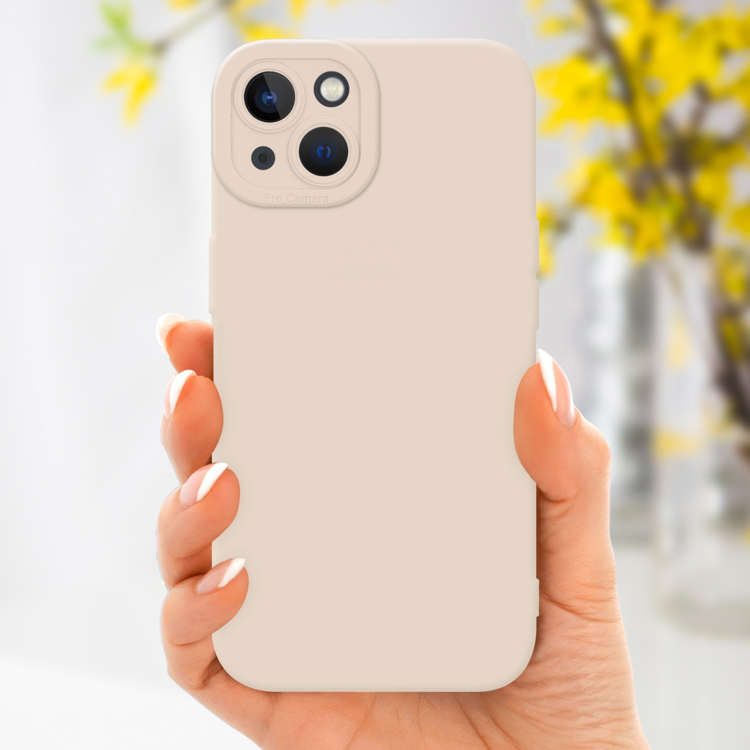 Mano che tiene una custodia beige per telefono. Tre obiettivi della fotocamera visibili. Fiori gialli sullo sfondo.