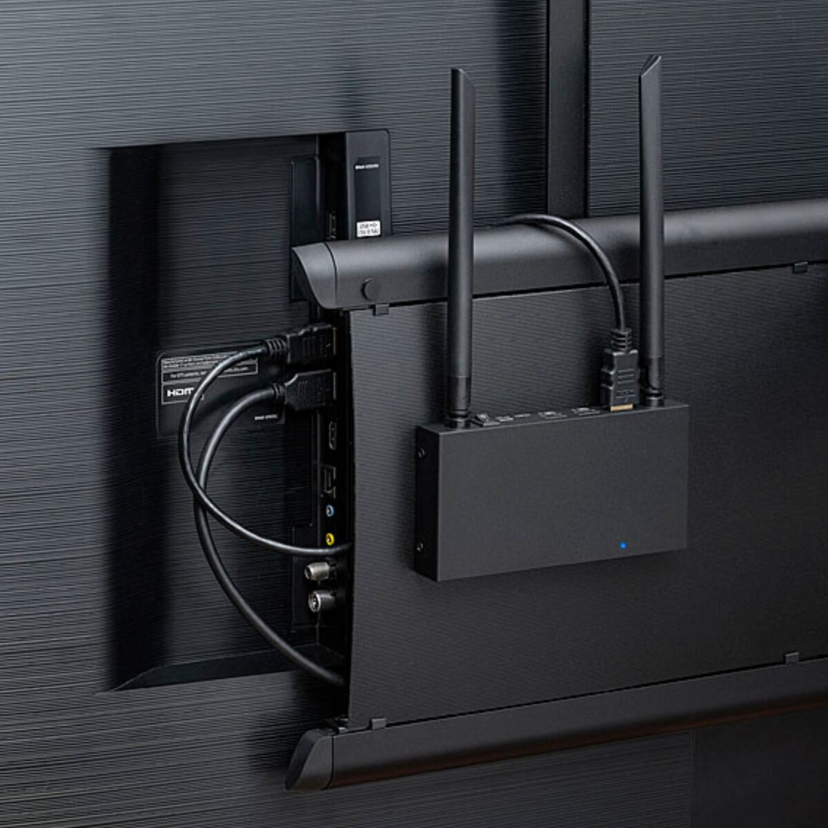 Back of a TV with a black receiver box, two antennas, and connected cables. 