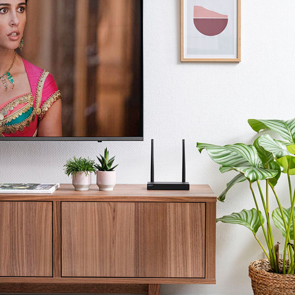 A TV, a router, and plants on a wooden cabinet against a white wall.