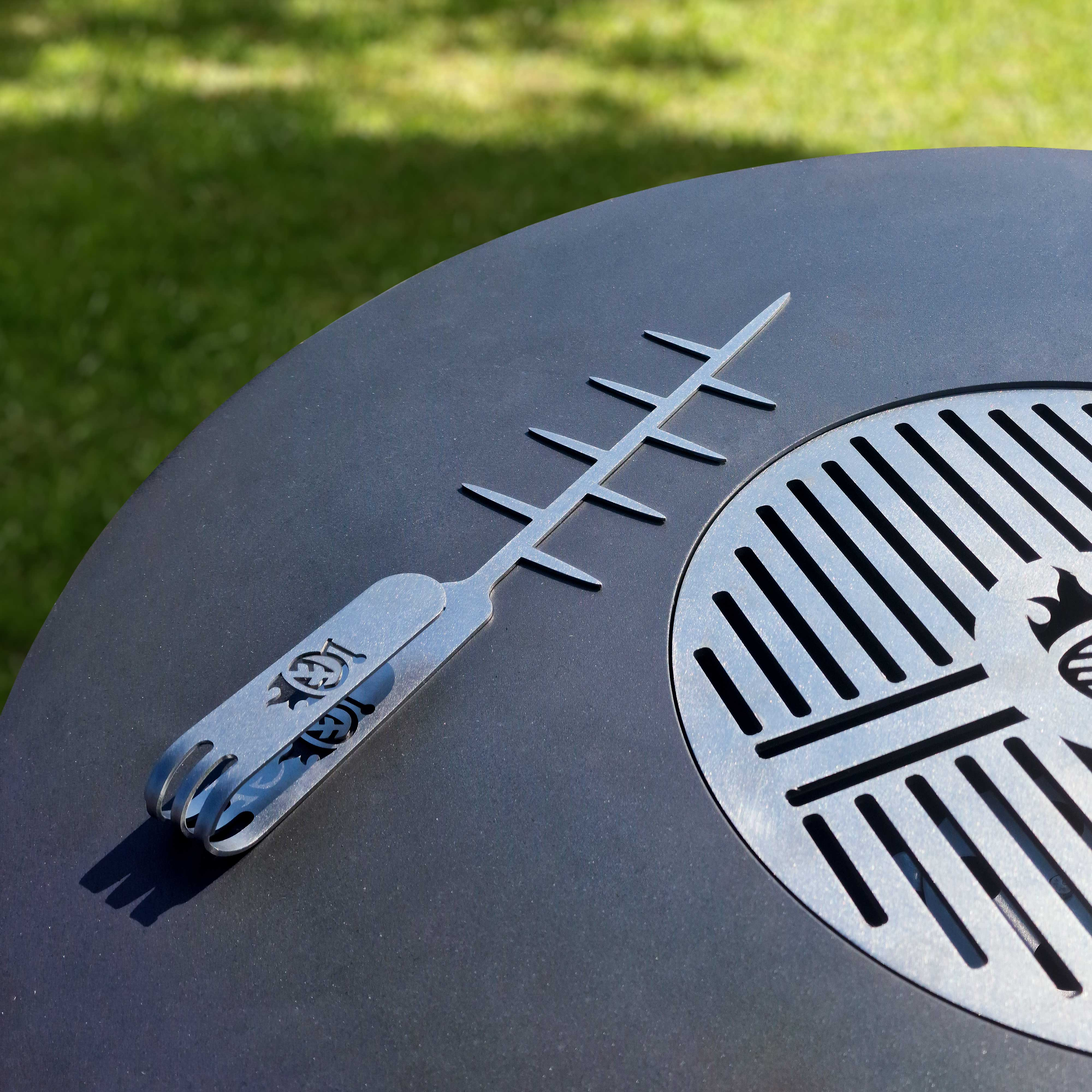 Metall-Grillwerkzeug auf schwarzer Oberfläche. Grilldesign. Grüner Grashintergrund.