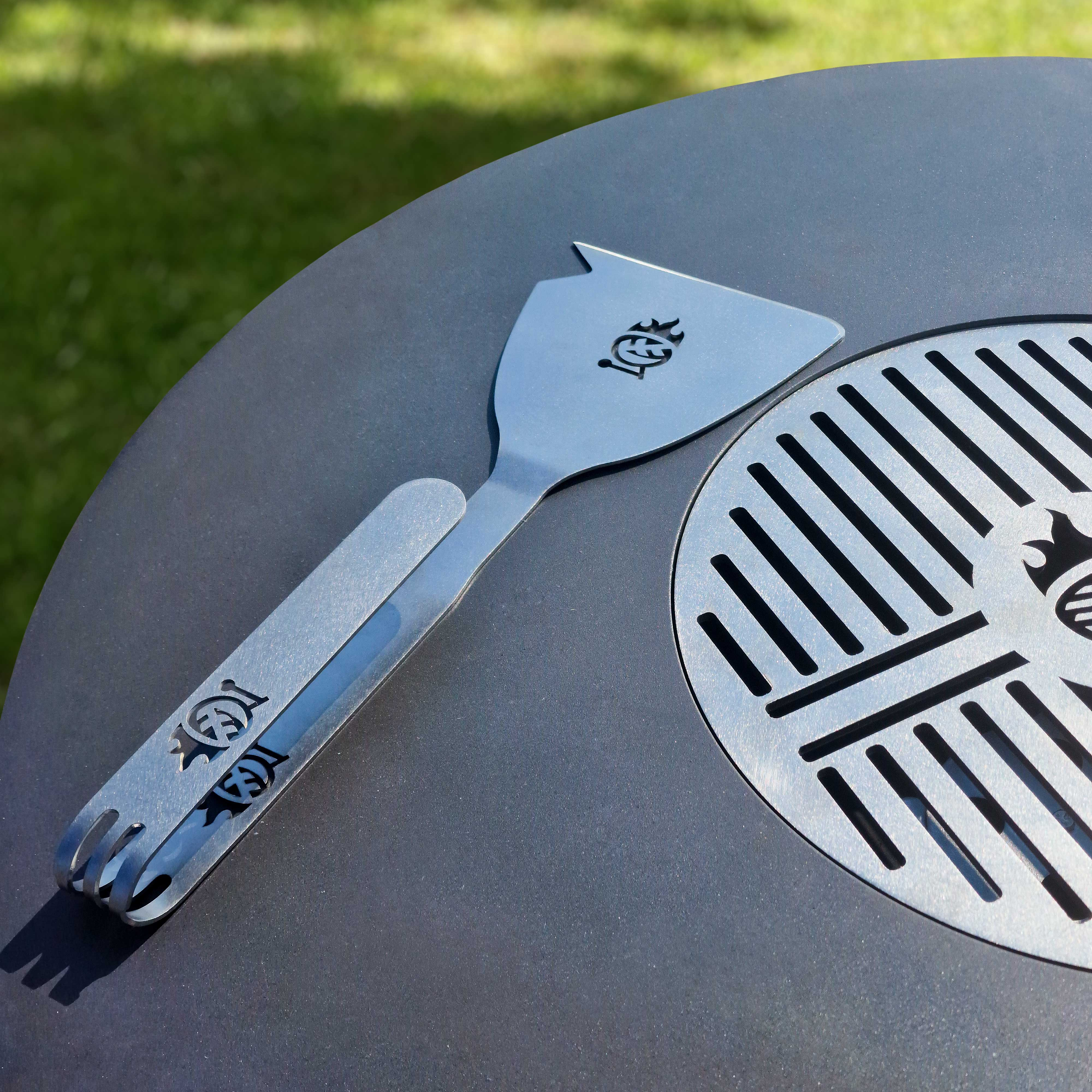 Ein Edelstahl-Pfannenwender auf einem Grill, Nahaufnahme.