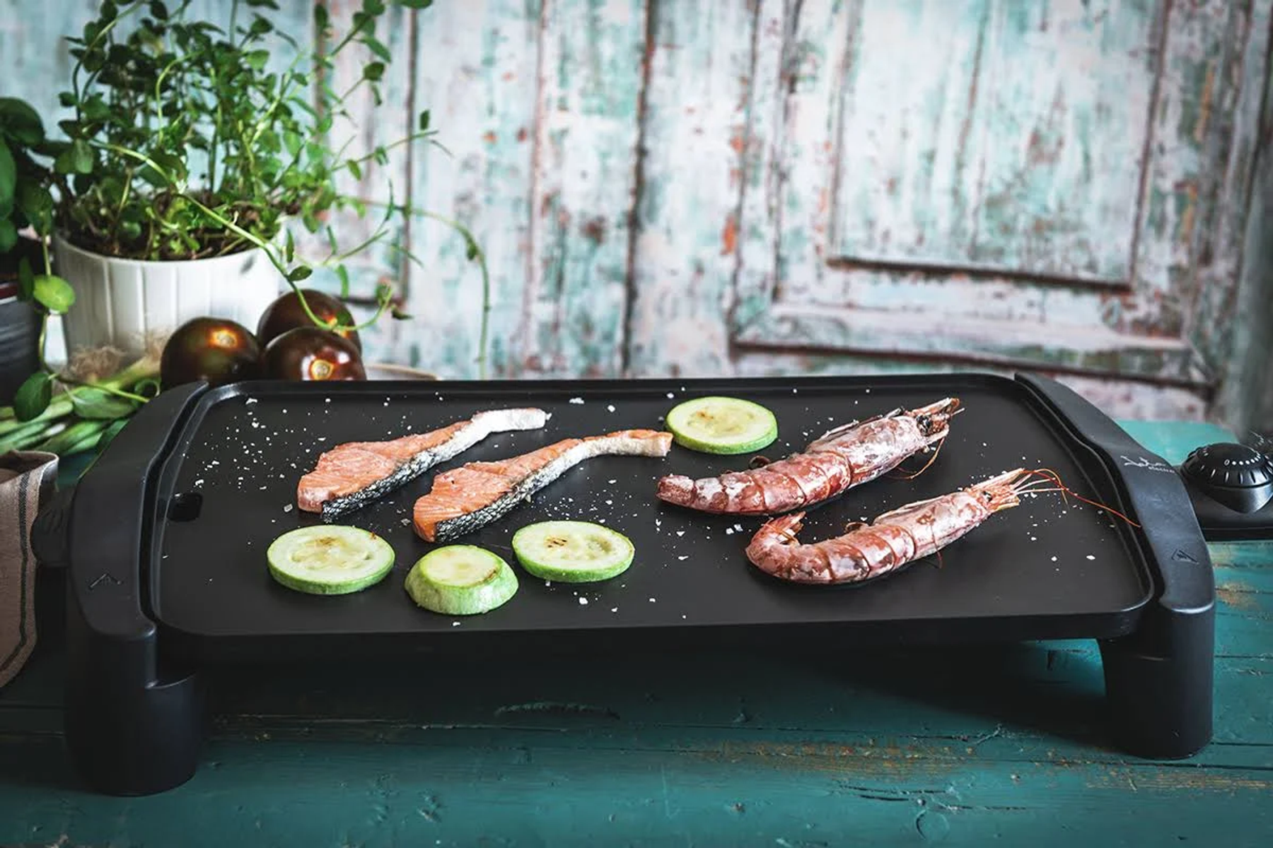 Parrilla eléctrica con salmón, camarones y calabacín. Ingredientes en la parrilla. Fondo verde.