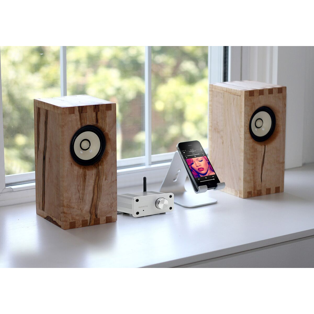 Deux enceintes en bois avec des haut-parleurs blancs. Un téléphone sur un support entre les deux avec un câble blanc.