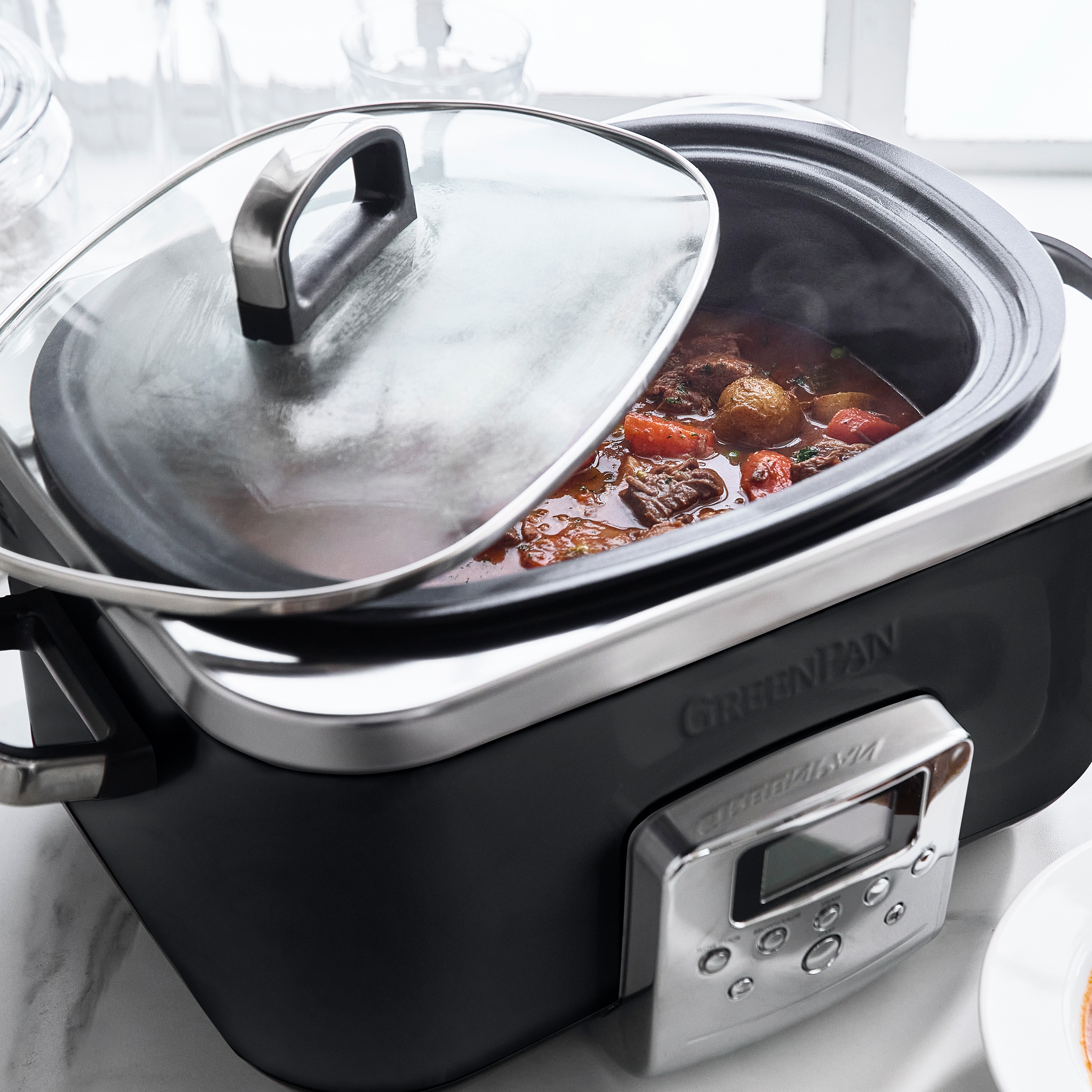 Ein schwarzer und silberner Slow Cooker, dessen Deckel teilweise geöffnet ist und Eintopf zeigt. Digitalanzeige.