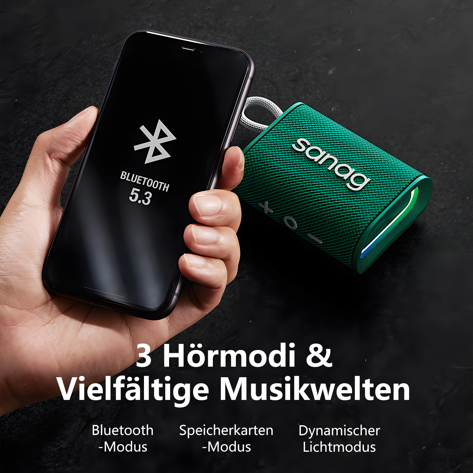 Eine Hand hält ein schwarzes Smartphone neben einem grünen Sanag Bluetooth-Lautsprecher.