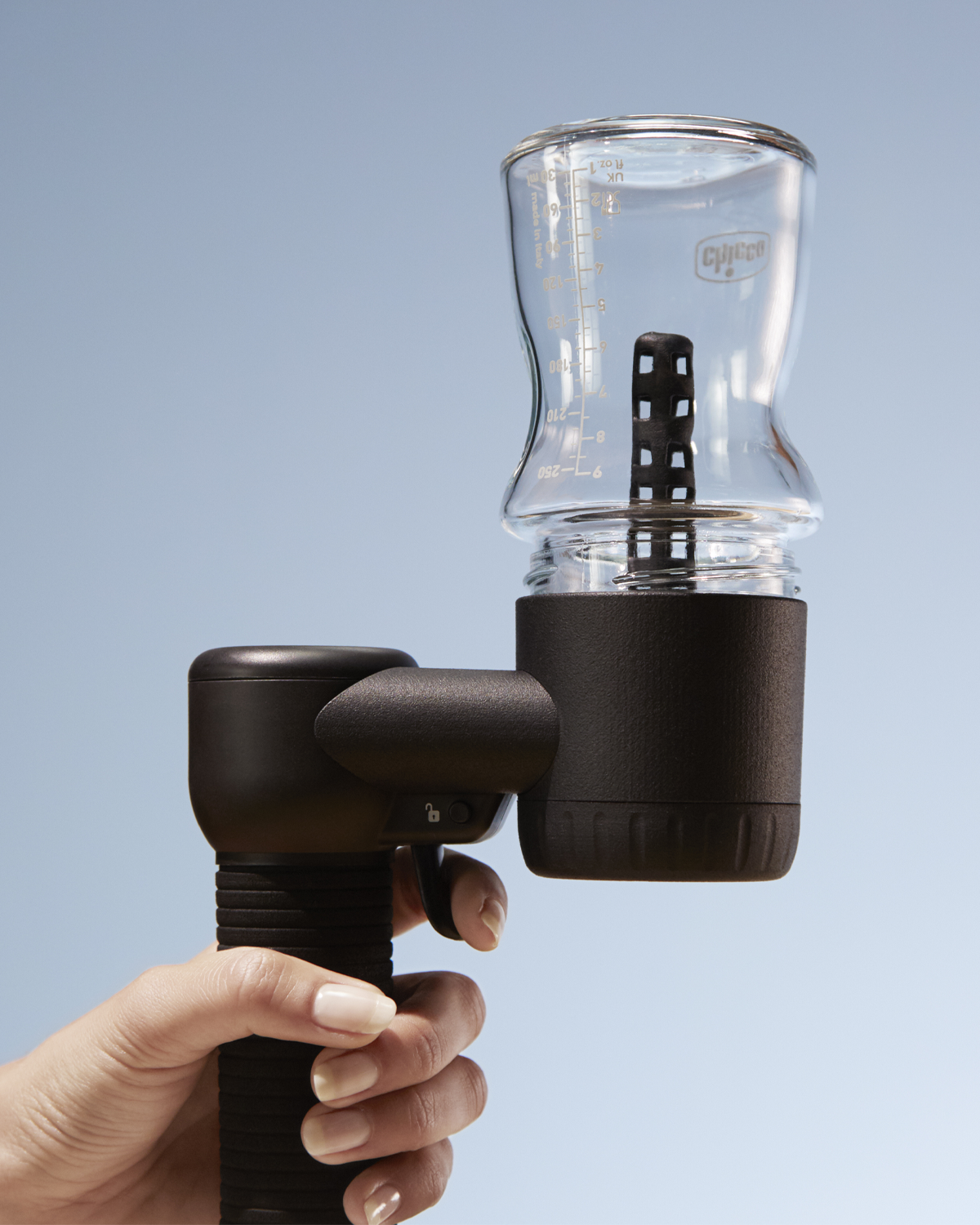 Eine Hand hält ein schwarzes Gerät mit einer durchsichtigen Glasflasche, vor blauem Hintergrund.