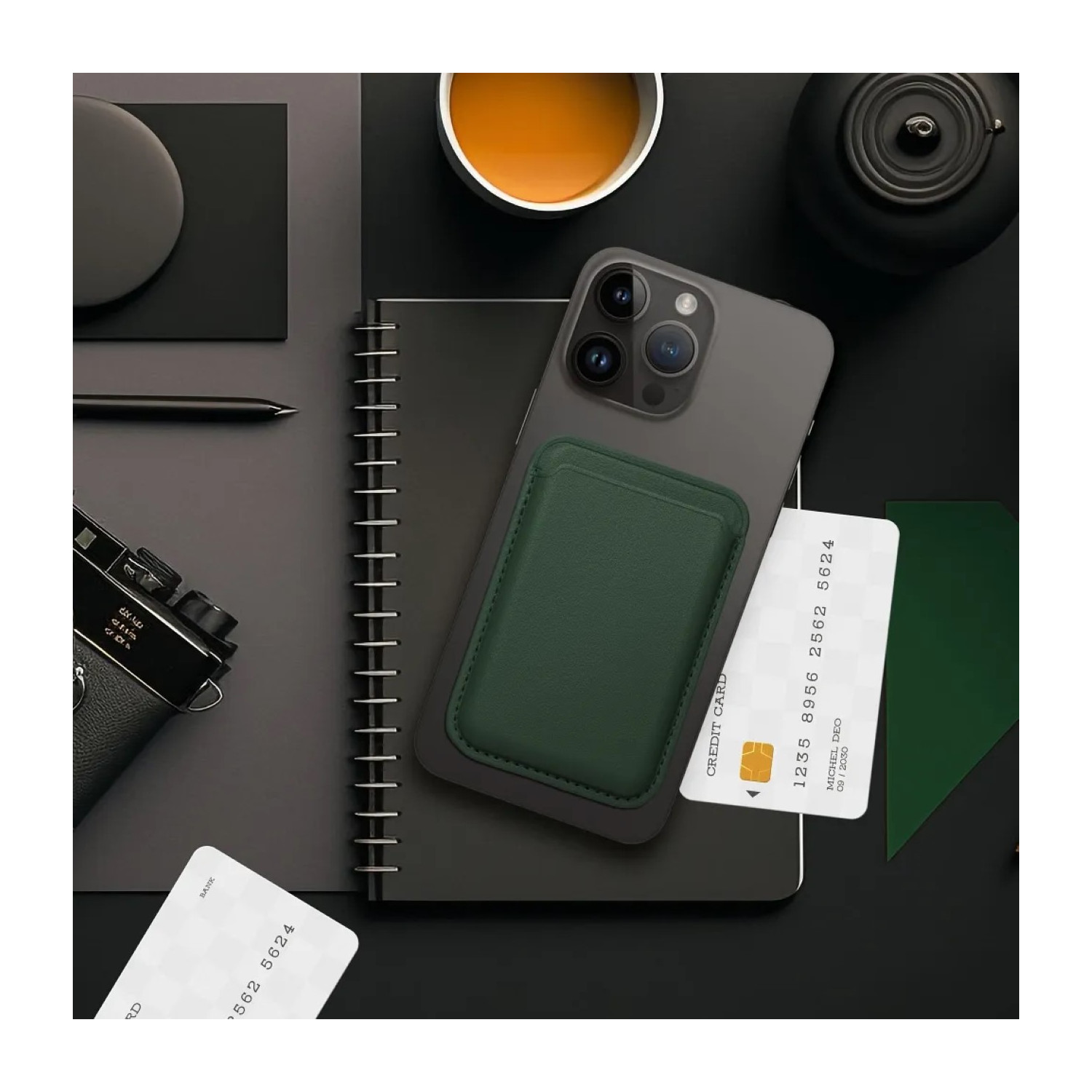 Un telefono con un porta carte verde attaccato, un taccuino, carte di credito e una fotocamera su una scrivania.