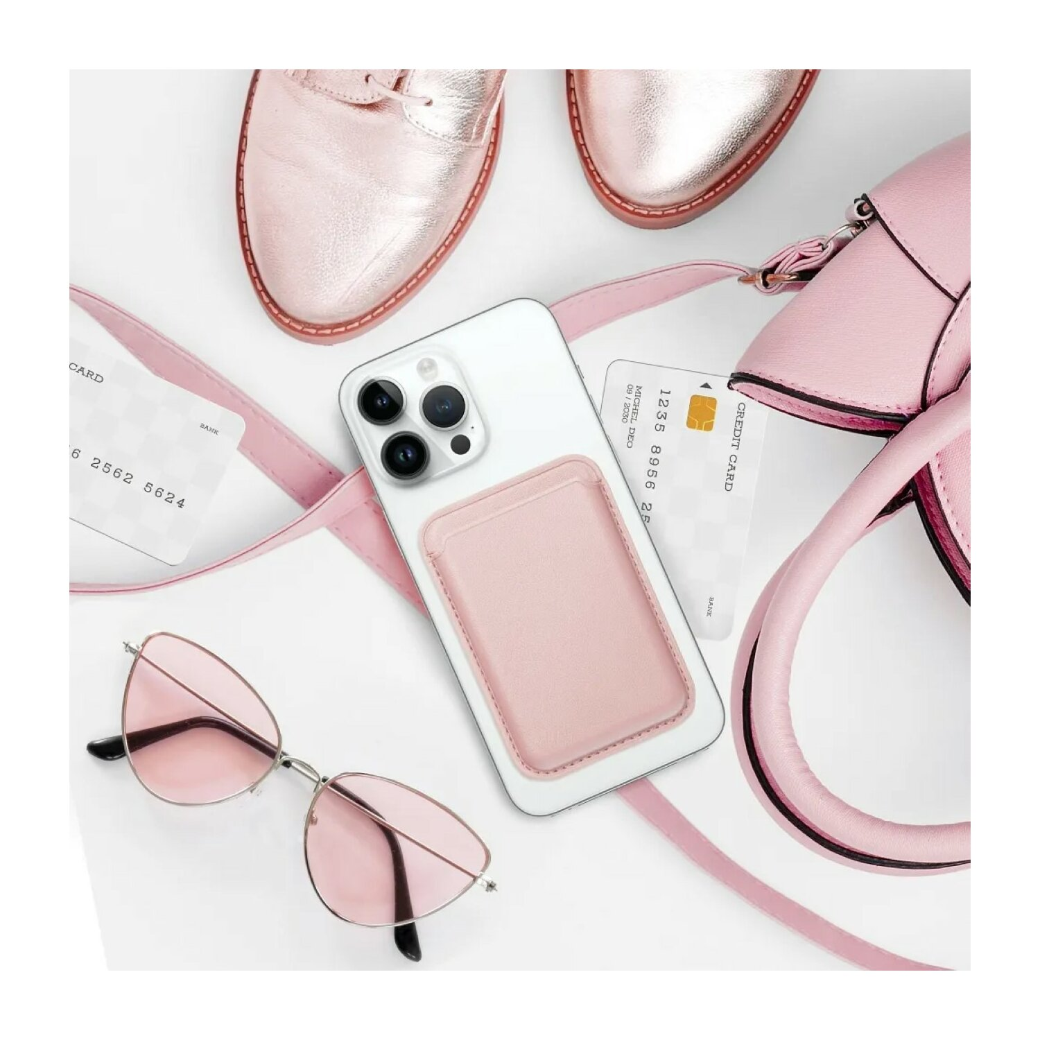 Un telefono con porta carte, carte, occhiali da sole e una borsa su una superficie bianca.
