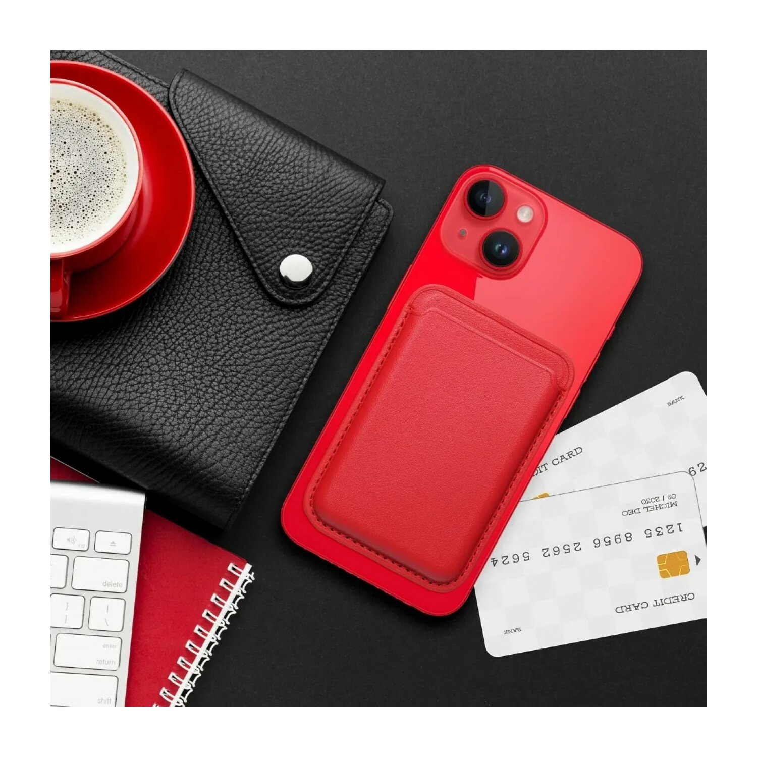 Un telefono rosso con un portafoglio, carta di credito, tazza di caffè e un taccuino su una superficie nera.