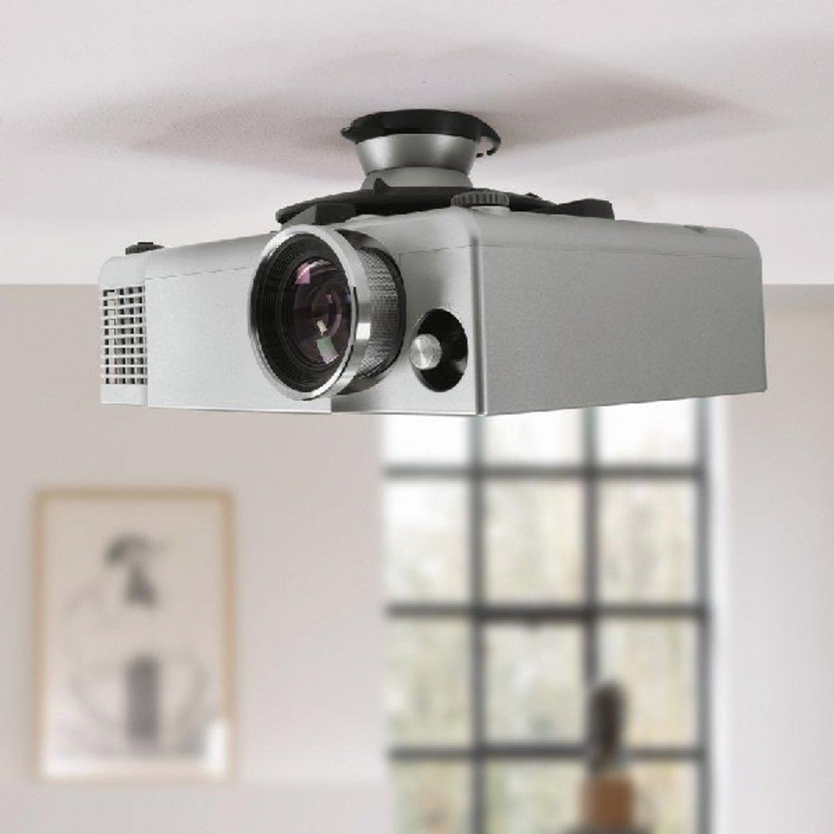 Srebrny projektor zamontowany na suficie, rzutujący w dół. Tło to jasny pokój.