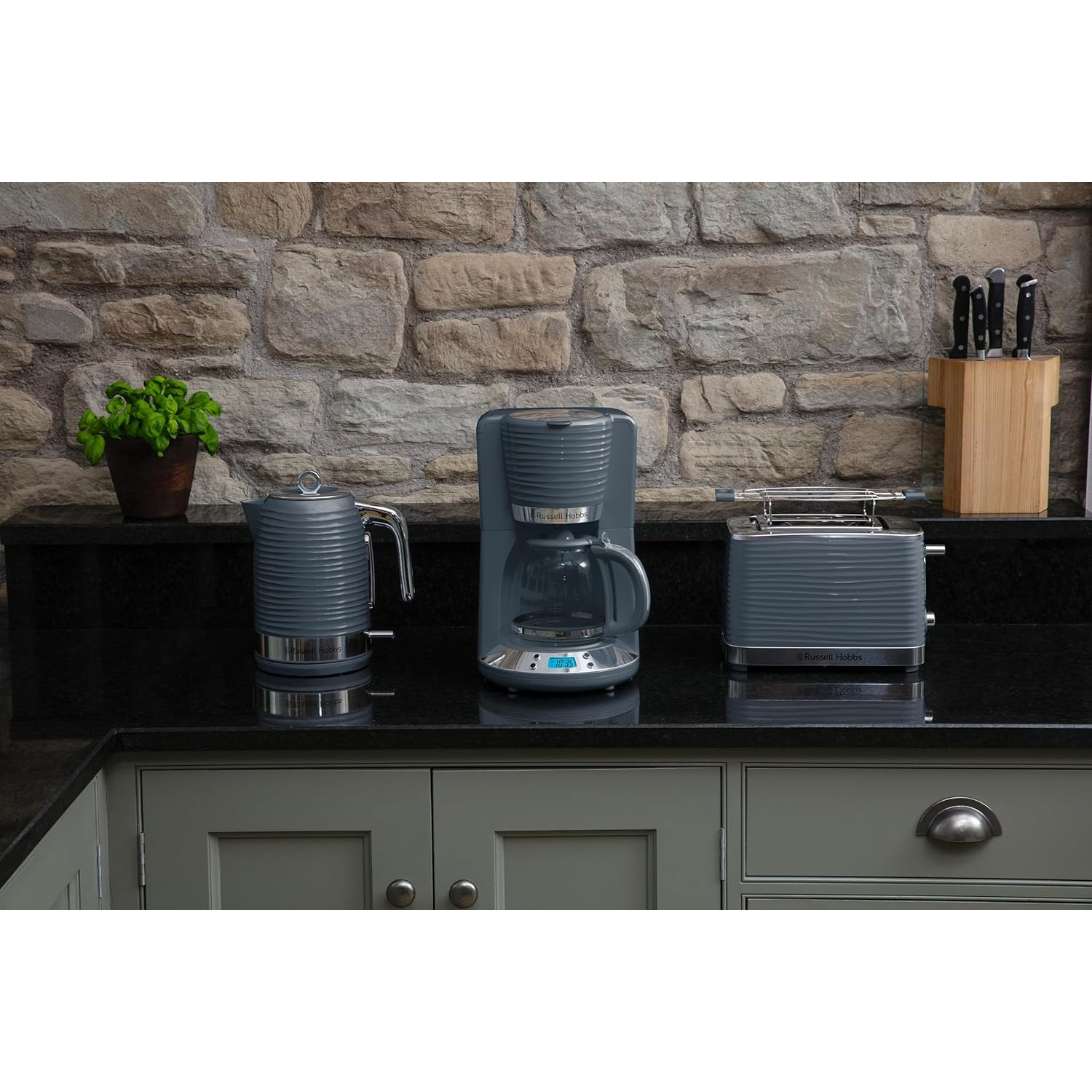 Encimera de cocina con hervidor, cafetera y tostadora grises. Fondo de pared de piedra.