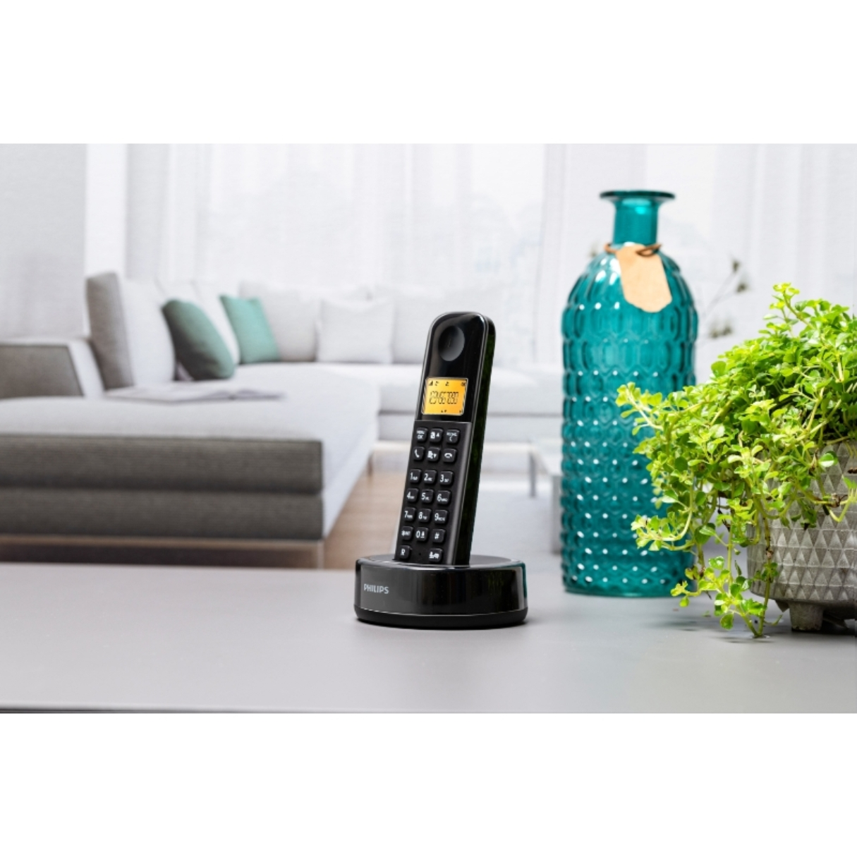 Téléphone sans fil sur une base. Il y a une plante verte et un vase bleu en arrière-plan.