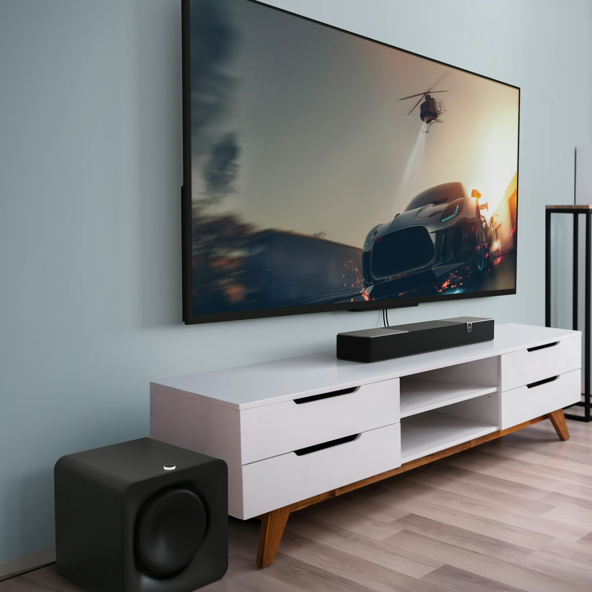 TV con scena inseguimento auto. Sotto soundbar, supporto bianco e subwoofer nero.