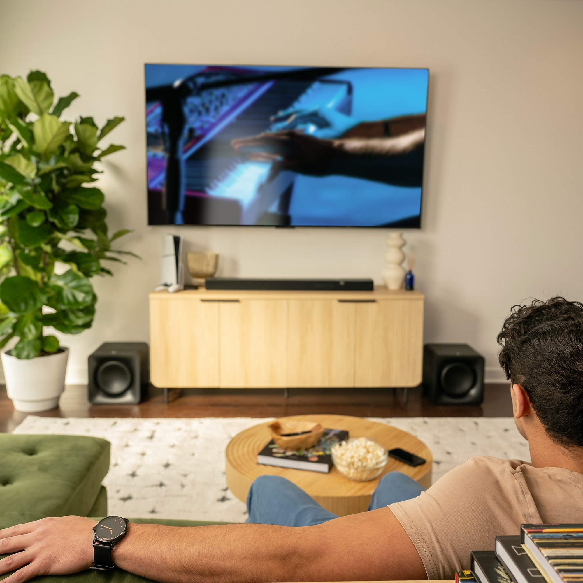 Una persona guarda la TV, con una soundbar su un mobile di legno e due subwoofer.
