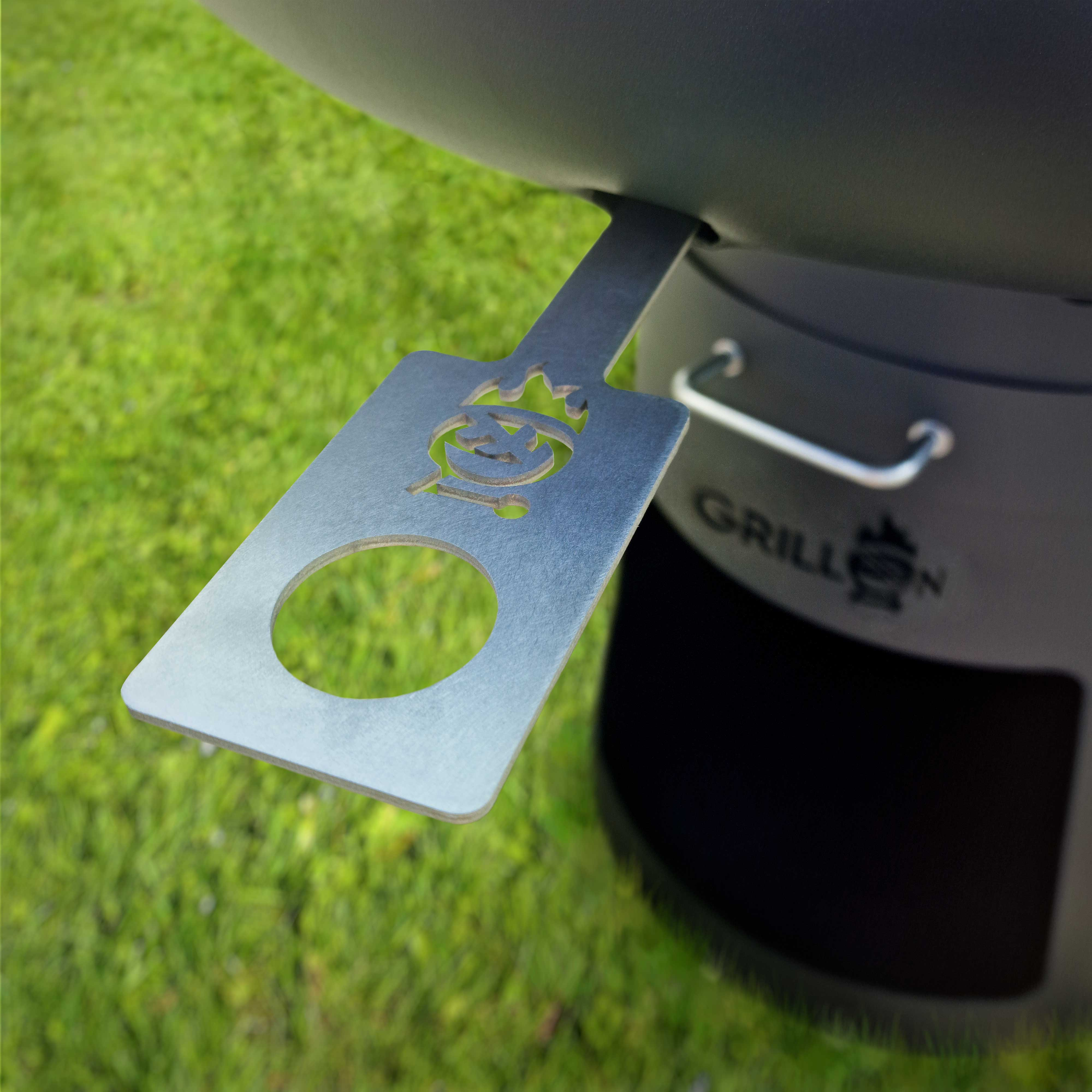 Metall-Grillzubehör. Grüner Gras-Hintergrund. Nahaufnahme des Grillaufsatzes mit Logo.