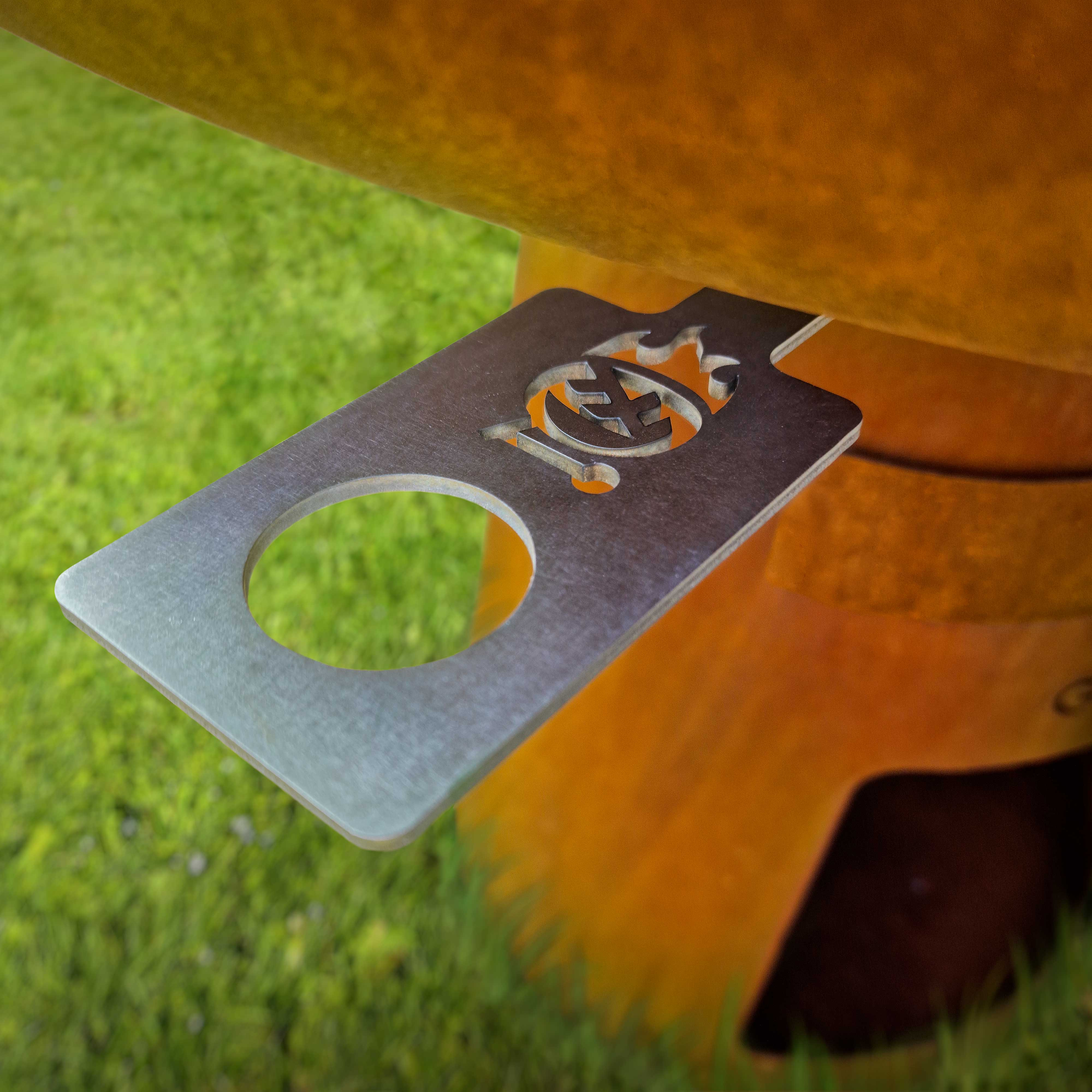 Ein Metallwerkzeug mit Loch auf einer orangefarbenen Oberfläche mit grünem Gras im Hintergrund.