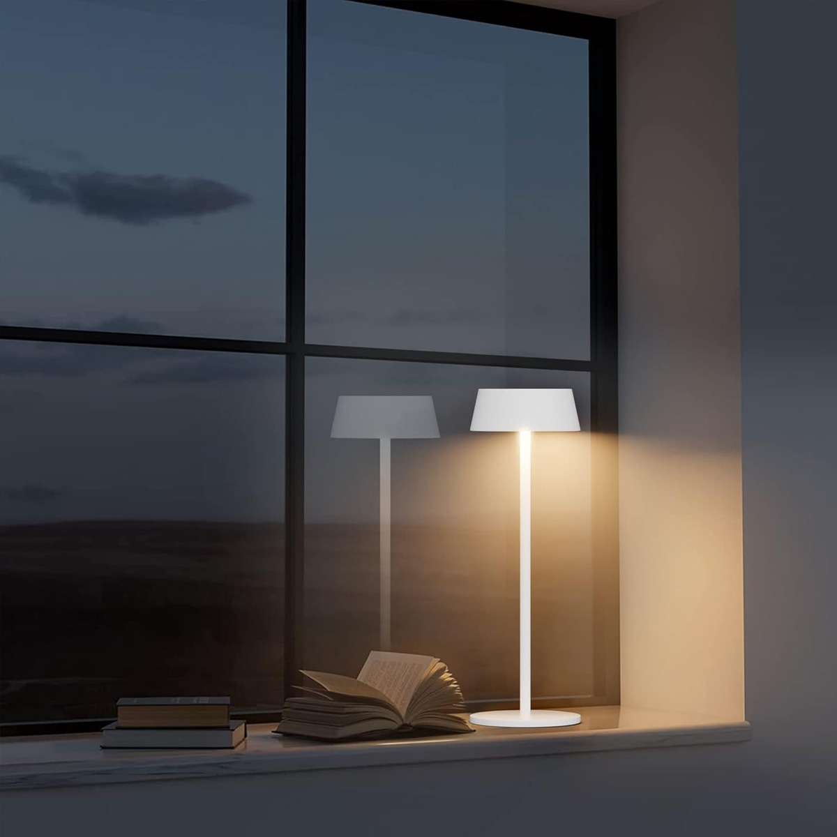 Weiße Lampe auf einer Fensterbank mit Buch und dunkler Nachtansicht draußen.
