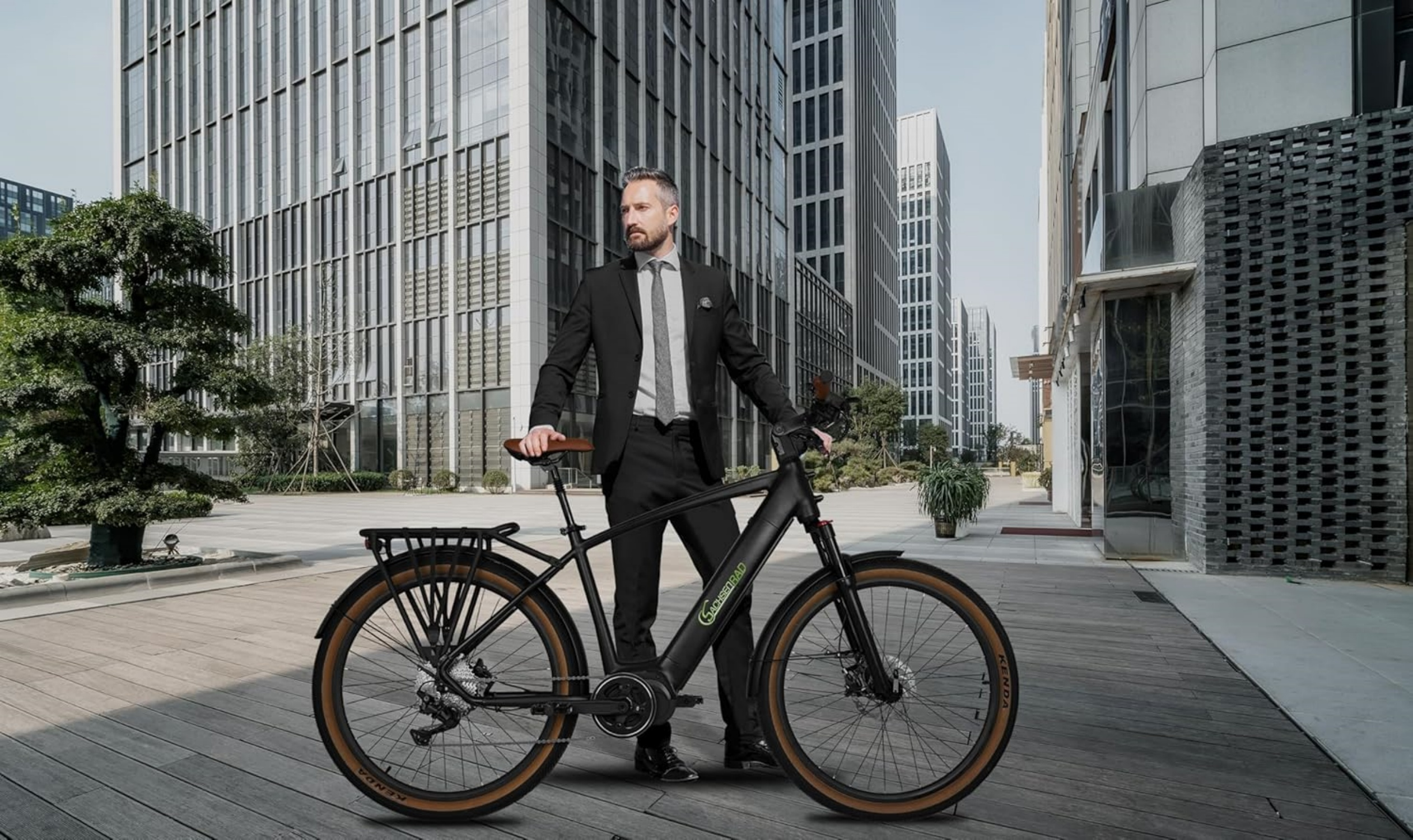 Mann im Anzug steht mit schwarzem Fahrrad auf einer Stadtstraße mit Gebäuden.