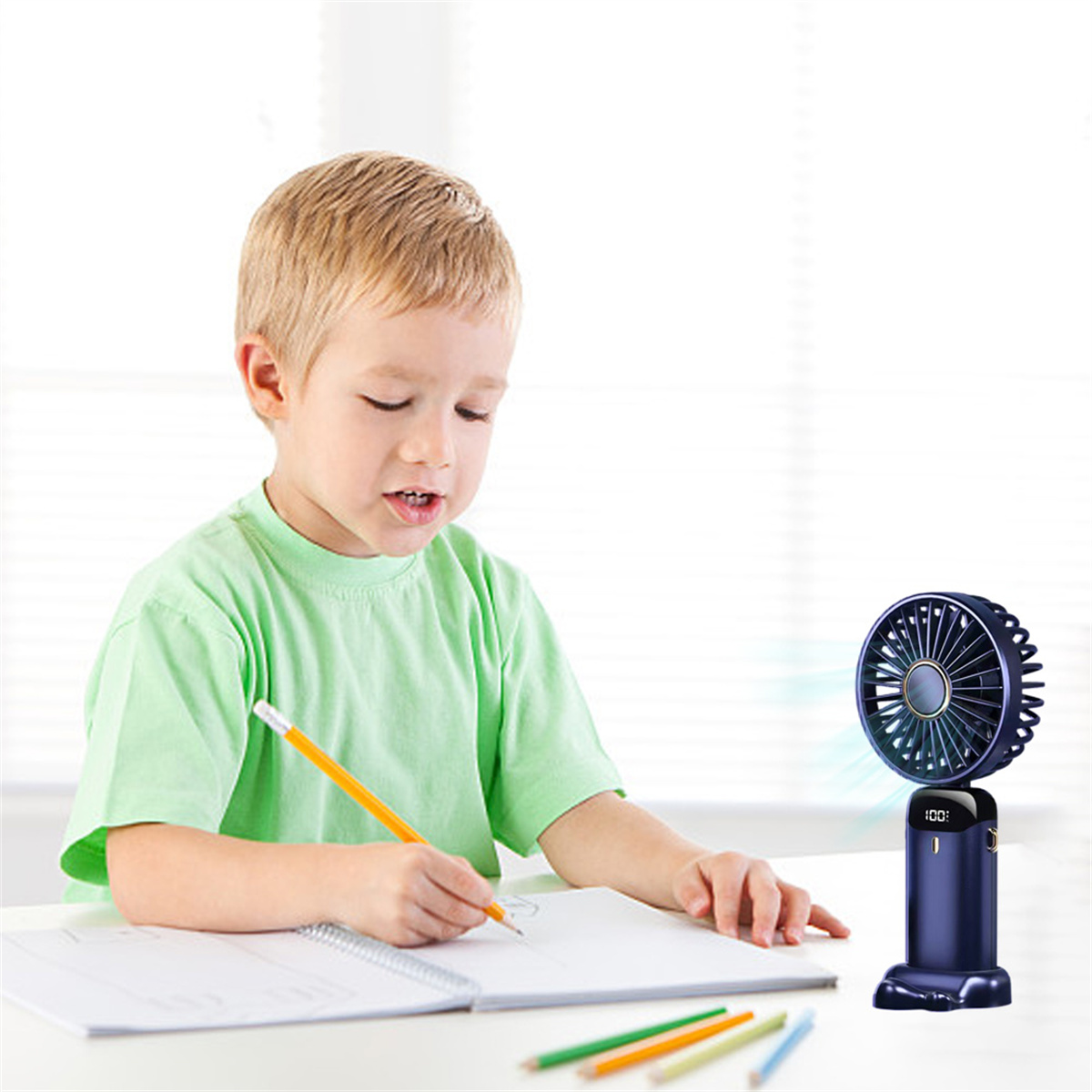 Ein Junge zeichnet mit einem Bleistift auf Papier, rechts ist ein kleiner Ventilator.