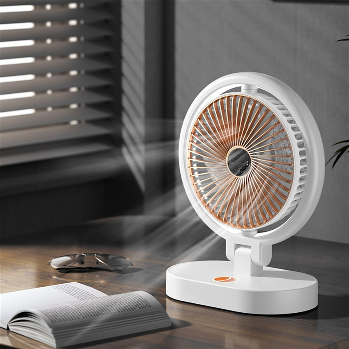 Weiß-goldener Ventilator auf einem Holztisch. Ein Buch und eine Brille im Vordergrund.