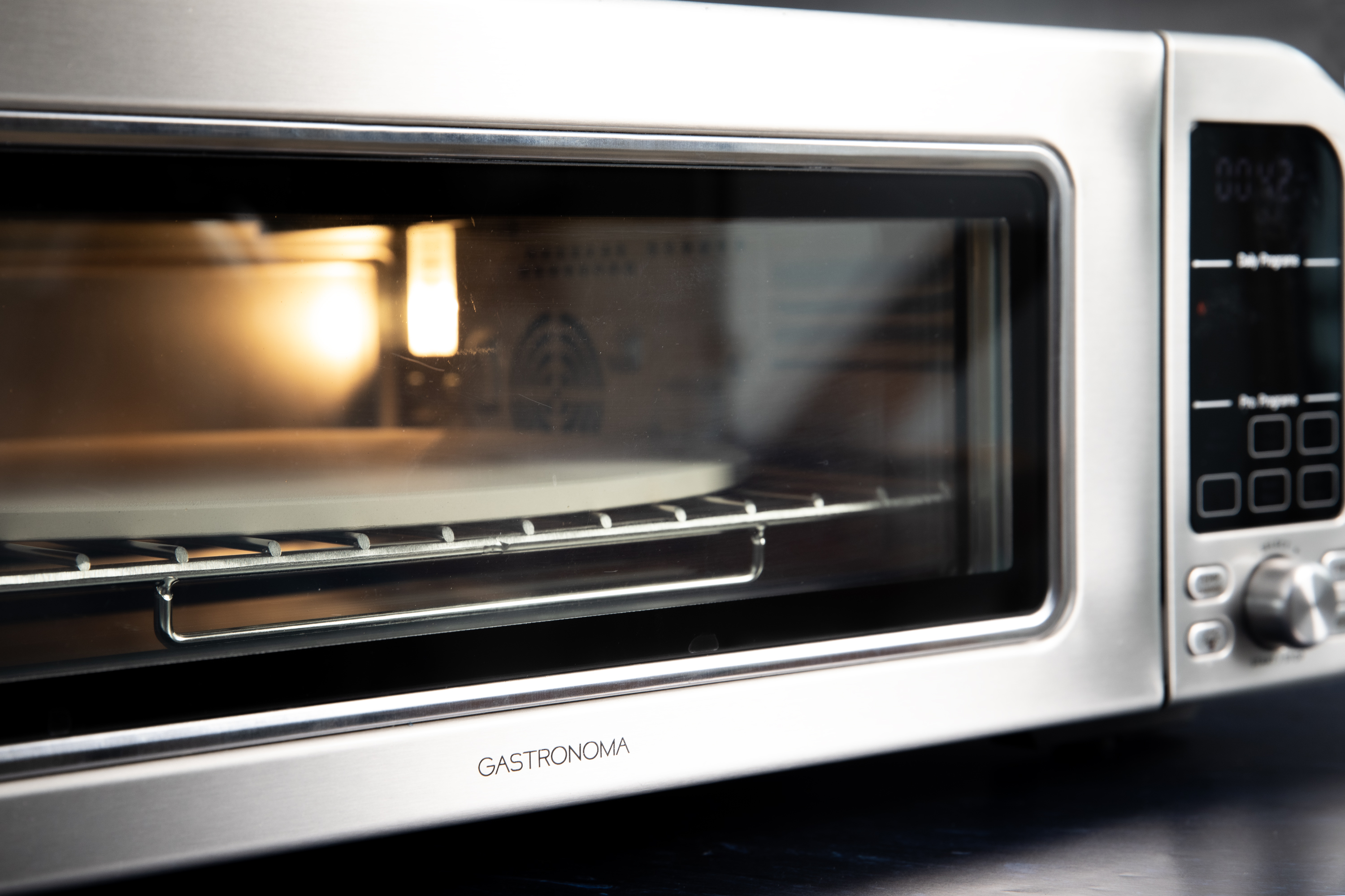 Srebrny piekarnik z tosterem ze szklanymi drzwiami. W środku kamień do pizzy.