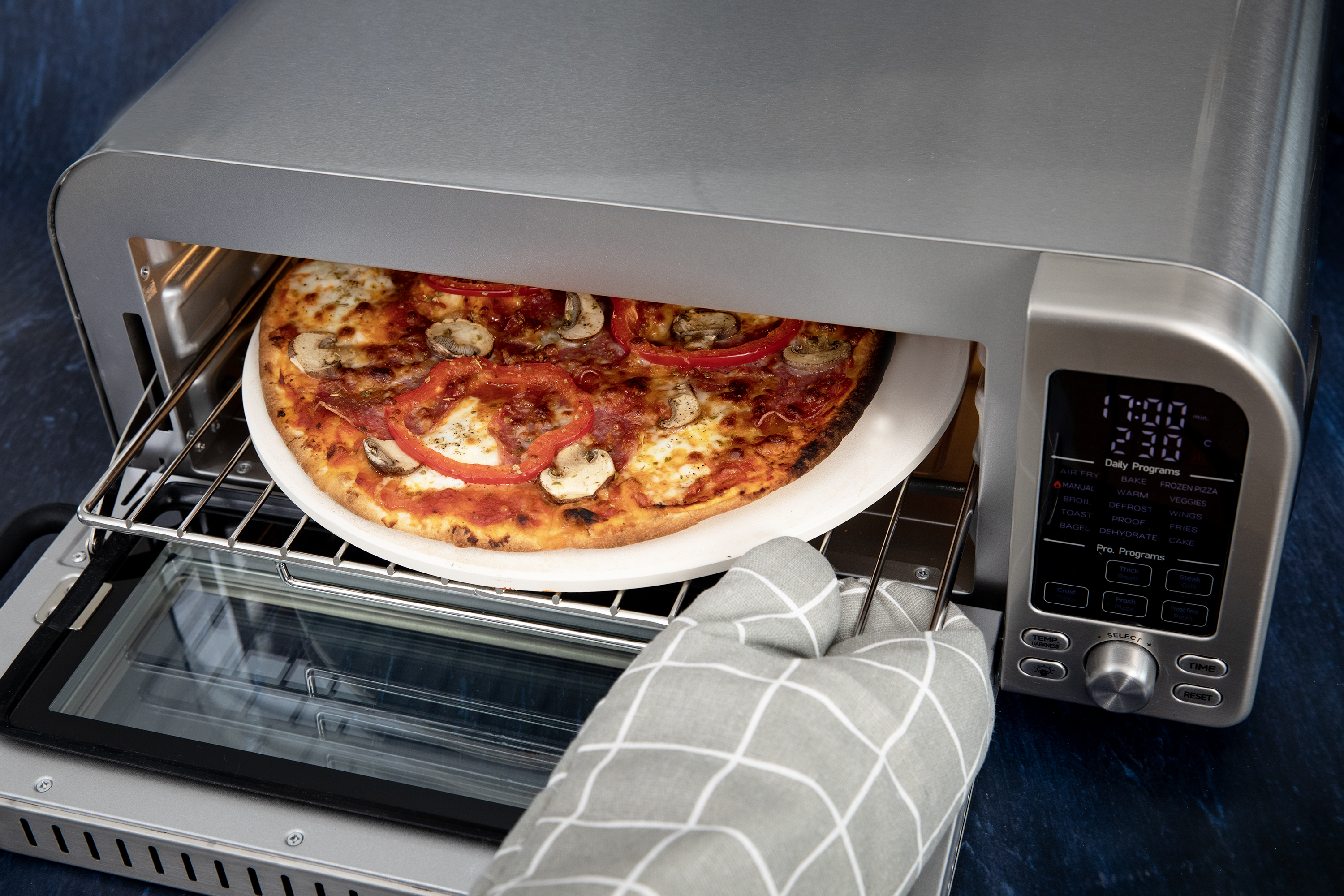 Pizza w piekarniku, z rękawicami kuchennymi trzymającymi tacę, cyfrowy wyświetlacz pokazujący czas.