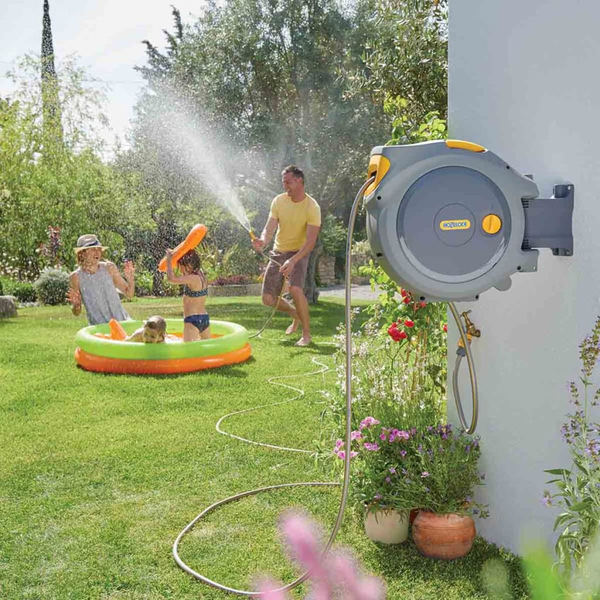 Familie spielt mit Wasser im Garten, mit einem Schlauch und Pool.