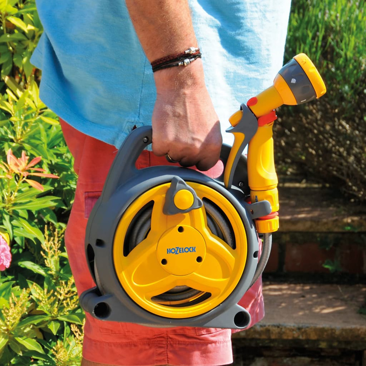 Person hält eine gelb-graue Schlauchtrommel und Düse in einem Garten.