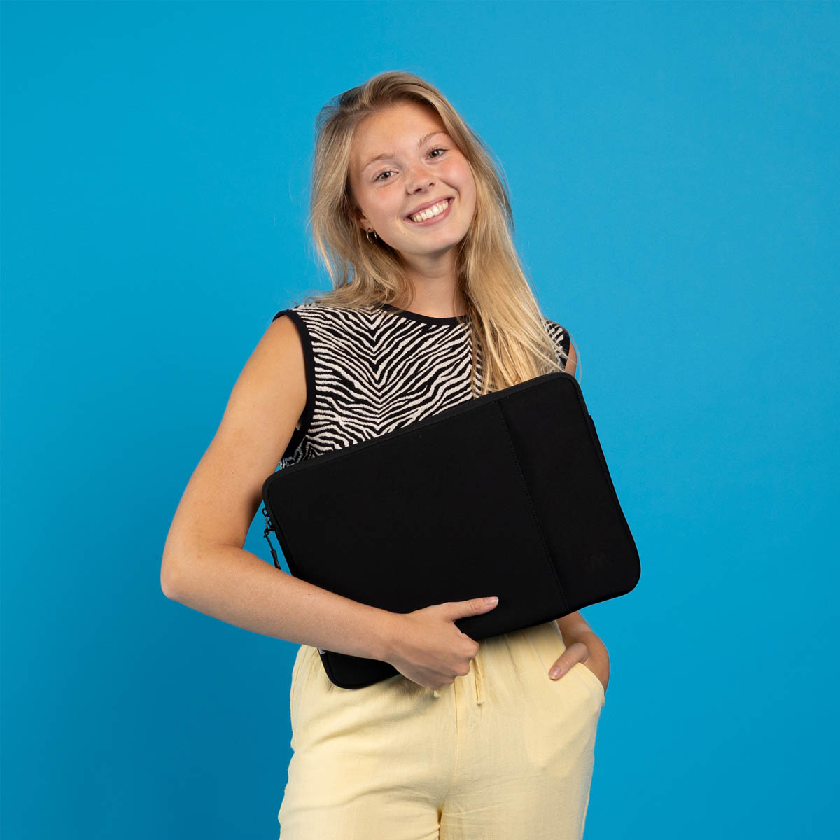 Woman holding a black laptop sleeve, smiling, blue background, zebra-striped shirt.