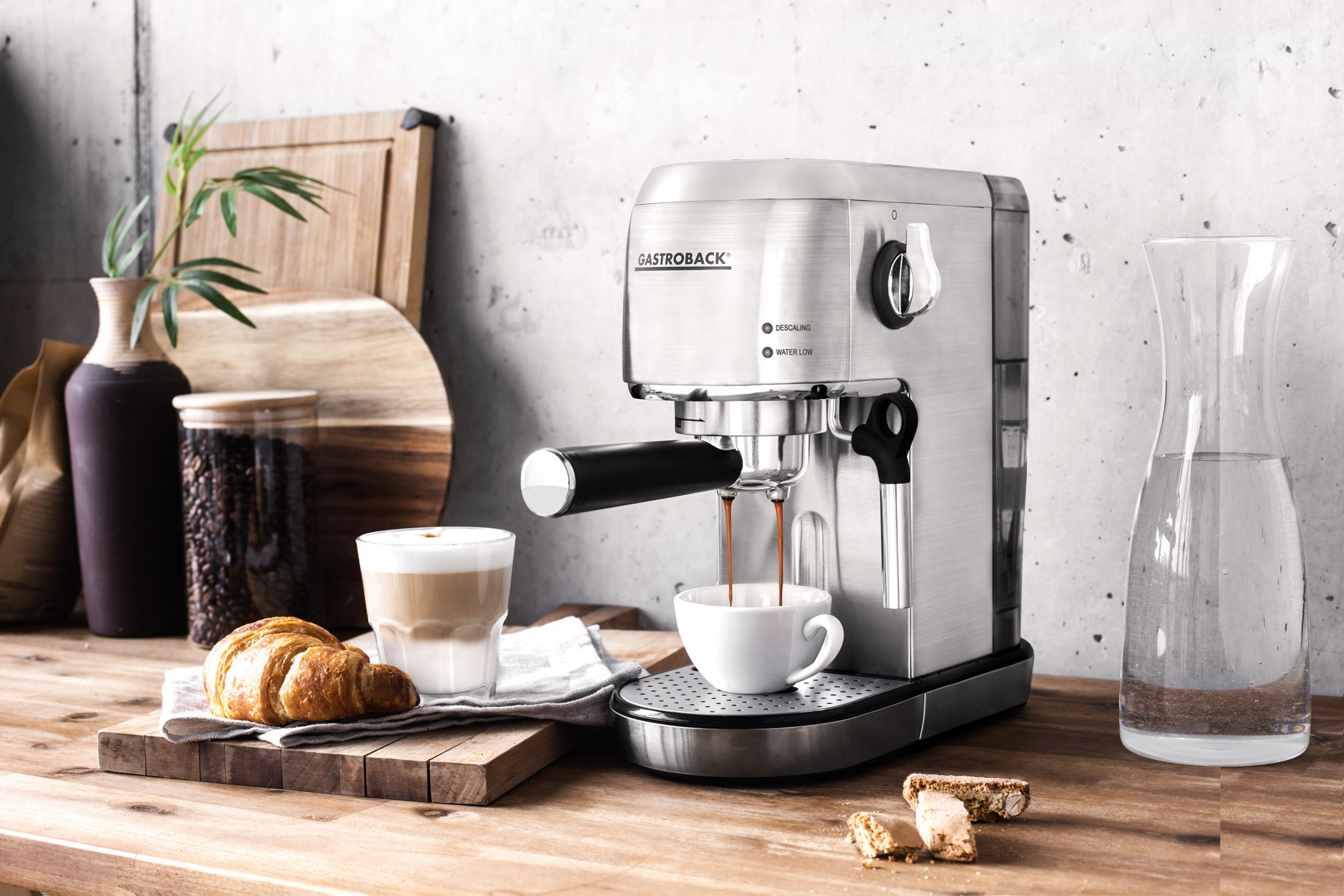 Ekspres do kawy z filiżanką, kawą i rogalikiem. Dzbanek z wodą stoi obok.