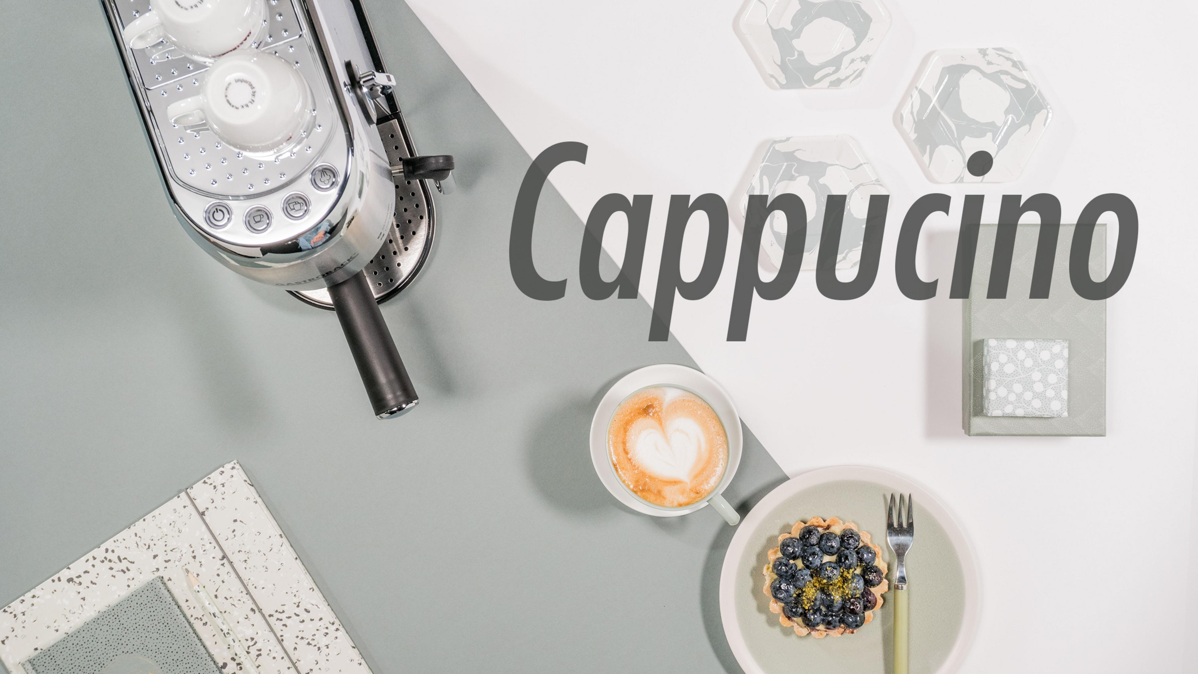 Ekspres do kawy, filiżanka cappuccino z sercem i tartą na stole. Tekst mówi 'Cappuccino'.