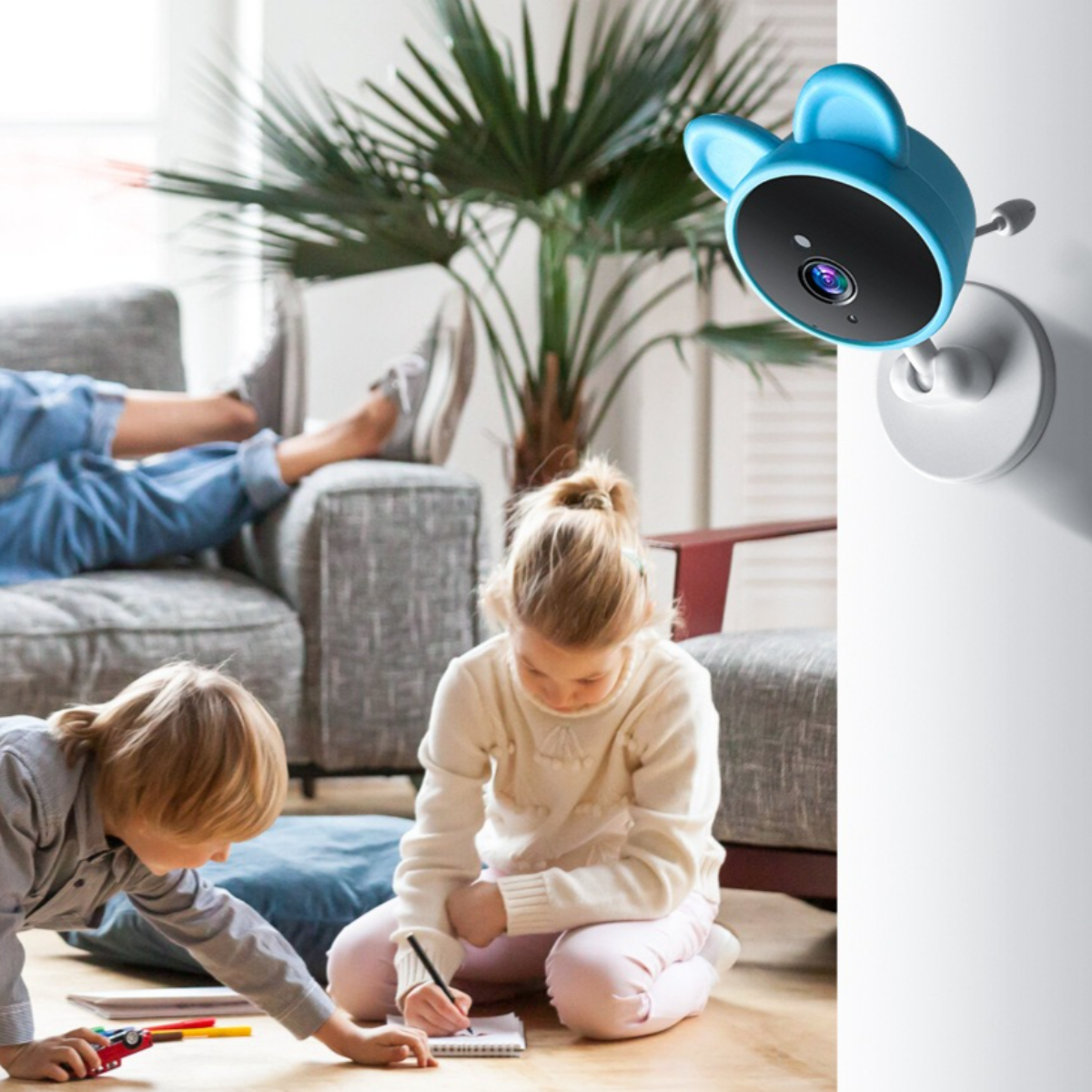 Zwei Kinder spielen mit Spielzeug auf dem Boden. Eine blaue Kamera im Hintergrund mit Ohren ist an der Wand befestigt.