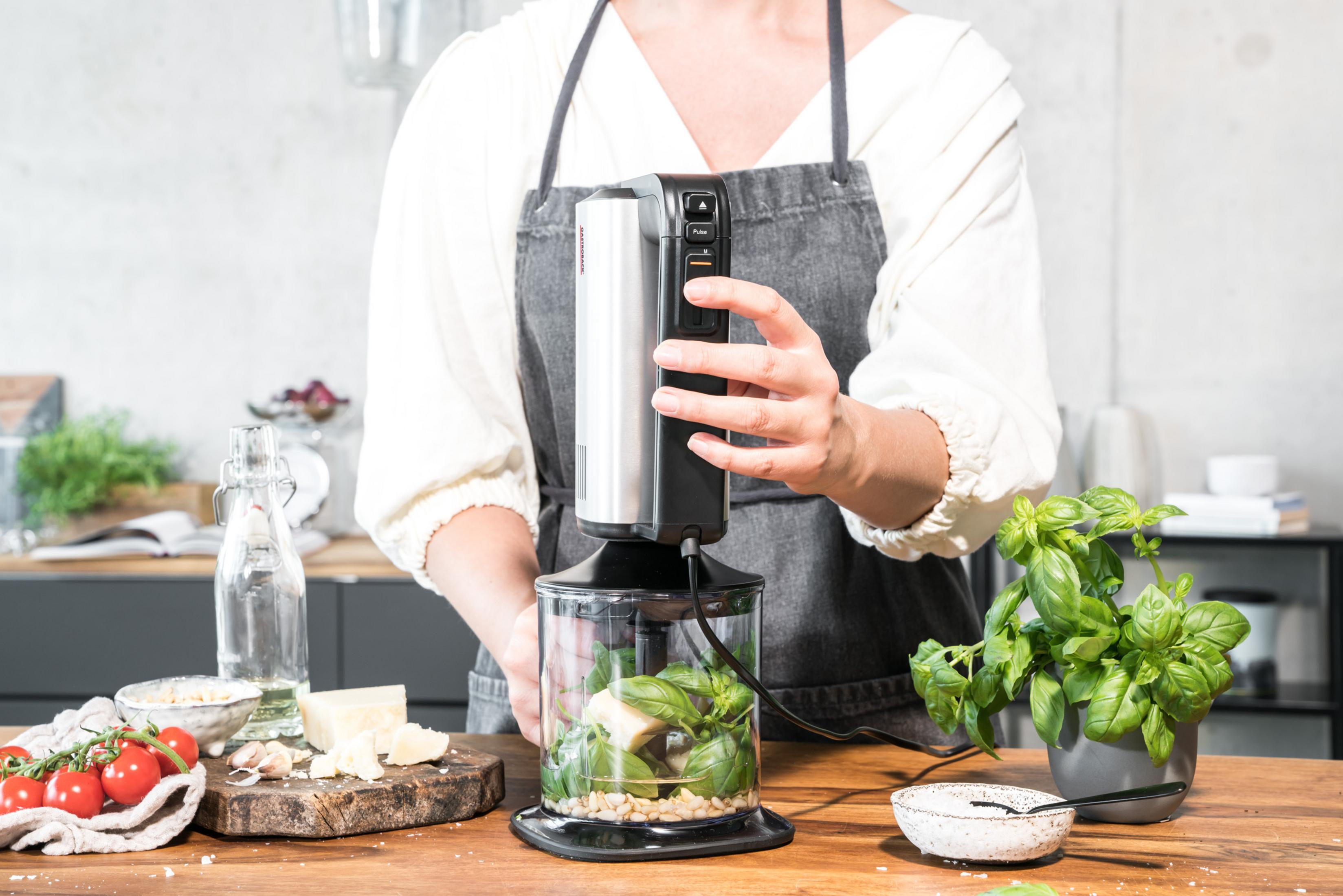 Una persona usa un frullatore a immersione per frullare gli ingredienti in un contenitore trasparente.