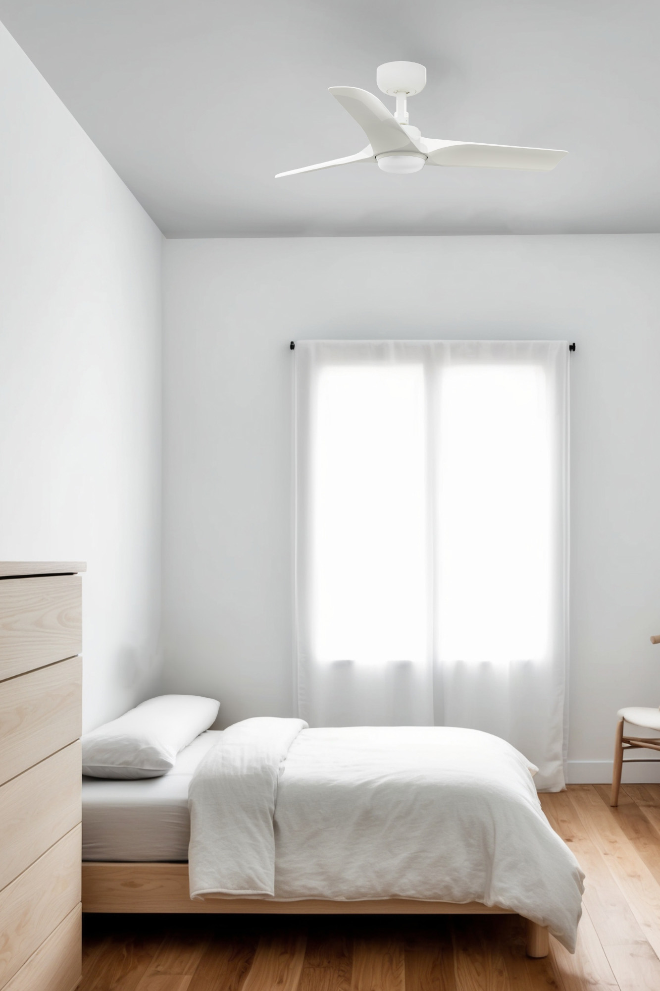 Ein Schlafzimmer mit weißen Wänden, Bett und Deckenventilator. Sonnenlicht scheint durch das Fenster.