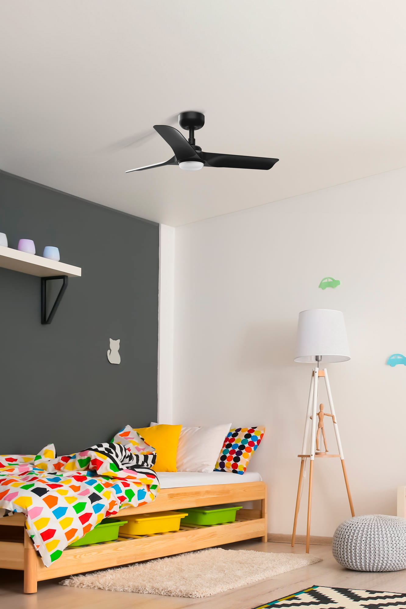 Un ventilatore a soffitto nero è montato nella camera da letto di un bambino. La stanza ha pareti bianche e grigie.