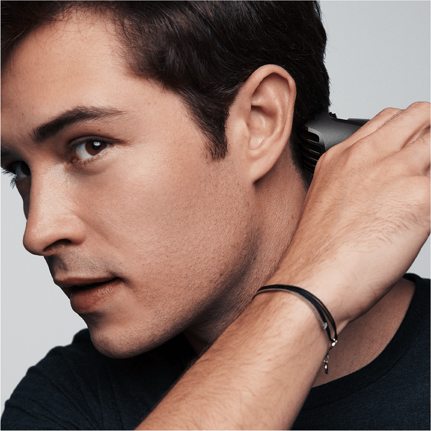 Man shaving his neck with a black trimmer. Close-up profile shot. Dark hair and bracelet.