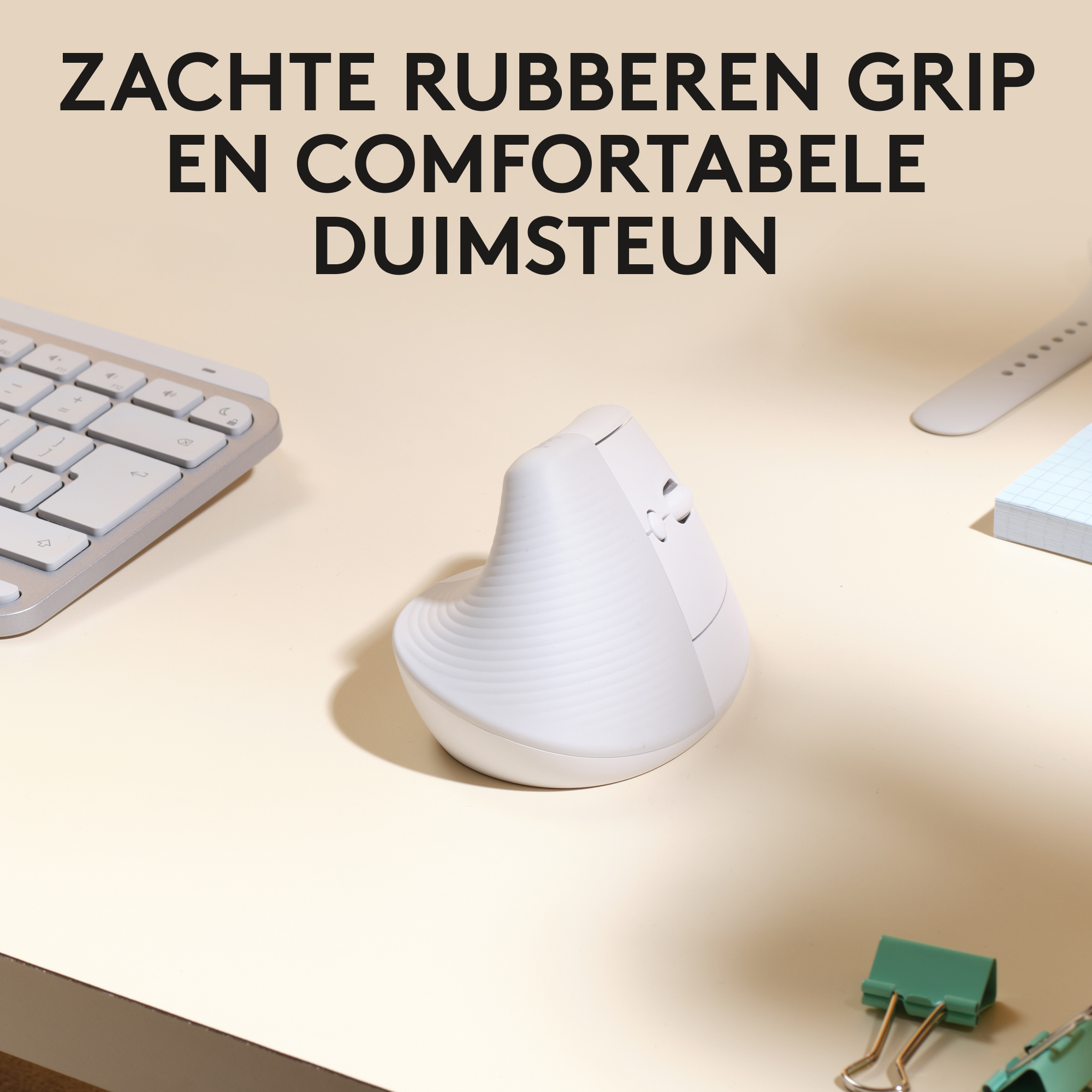 Biała, ergonomiczna mysz leży na jasnobeżowym biurku obok klawiatury, karteczek samoprzylepnych i spinacza.