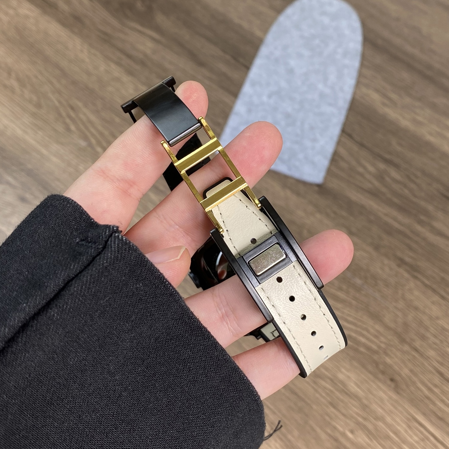Ein Uhrenarmband, schwarz mit goldenen Akzenten, gehalten von einer Hand auf Holz.