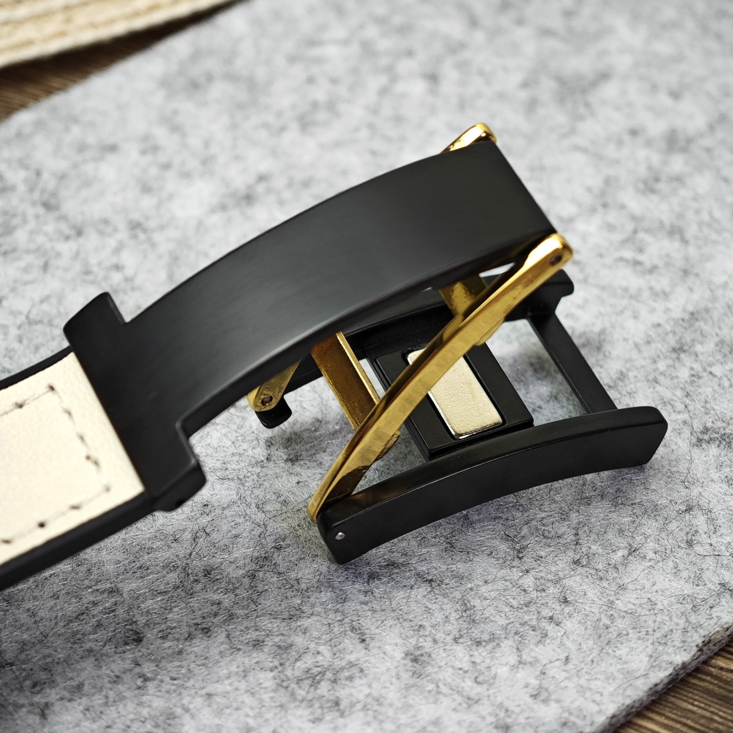 Nahaufnahme einer schwarzen Uhrenschließe. Gold- und schwarze Details. Auf grauer Oberfläche.
