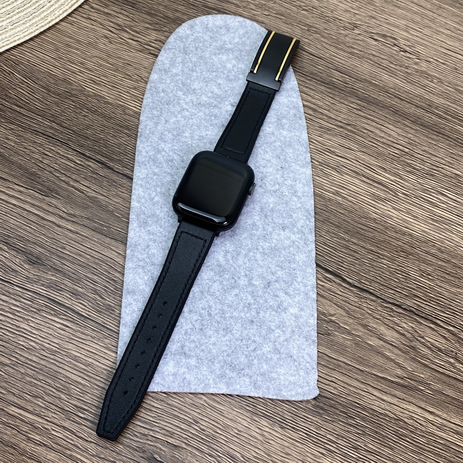 Eine schwarze Smartwatch mit Lederarmband liegt auf einem grauen Filzpad auf einer Holzoberfläche.
