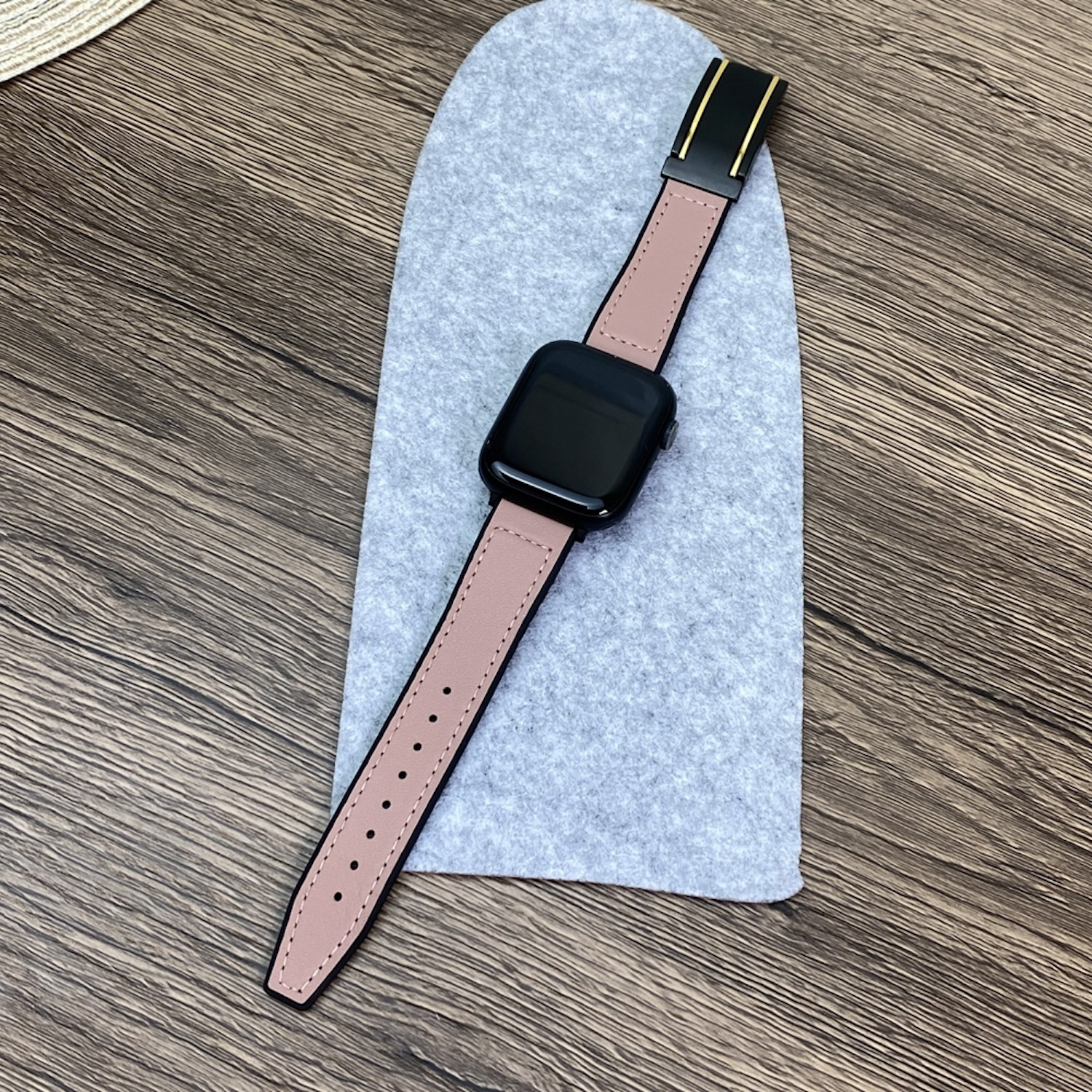 Smartwatch mit rosa Lederarmband, schwarzes Zifferblatt, auf grauem Filzpad.