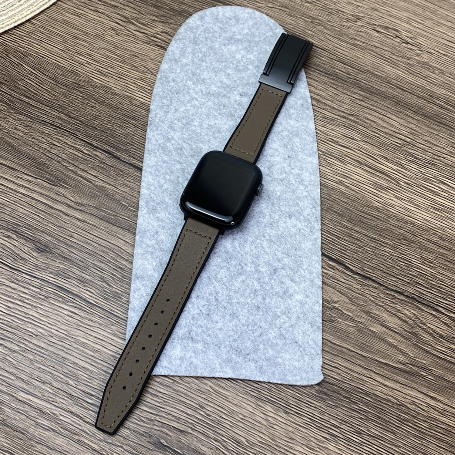 Smartwatch mit Lederarmband auf einer Filzoberfläche, die auf einem Holztisch liegt.
