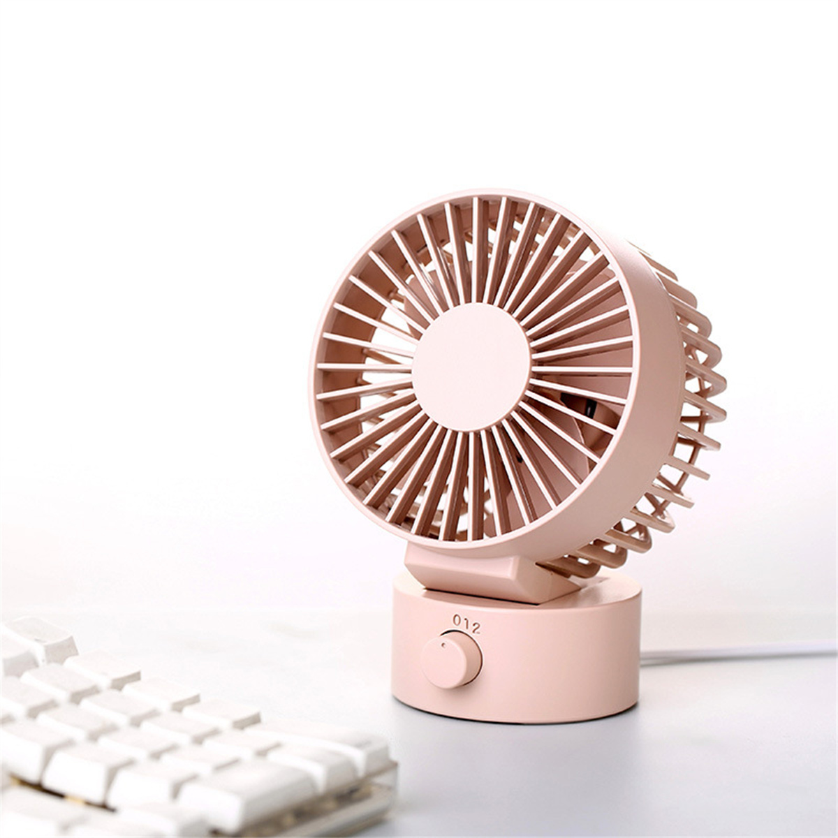 Ein kleiner rosa Ventilator mit rundem Kopf und Basis. Im unscharfen Vordergrund ist eine weiße Tastatur sichtbar.