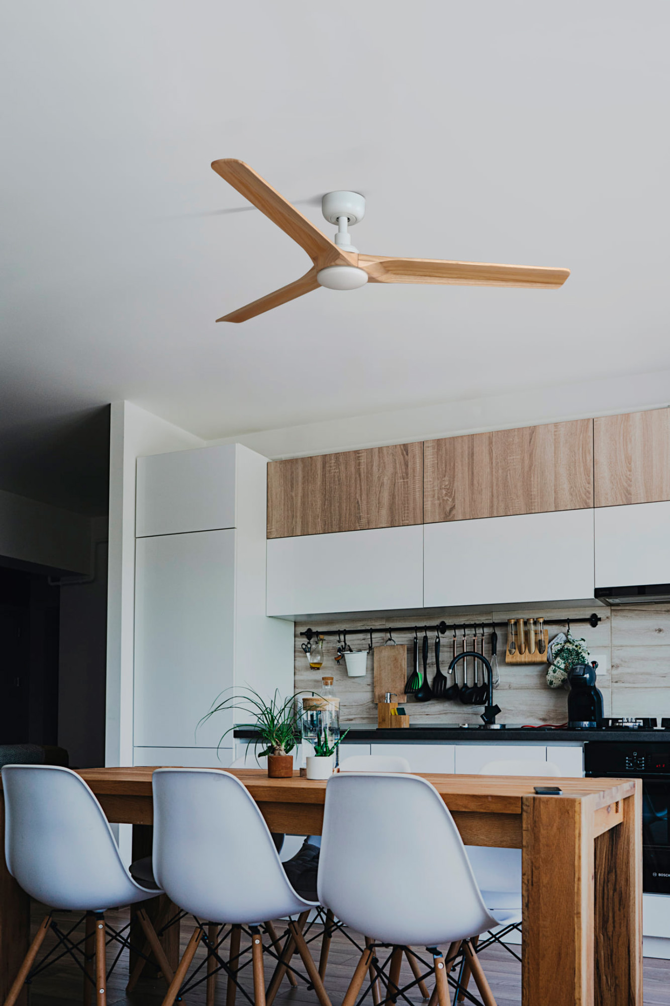 Küche mit weißen Schränken, einem Holztisch und einem Deckenventilator. Weiße Stühle sind vorhanden.