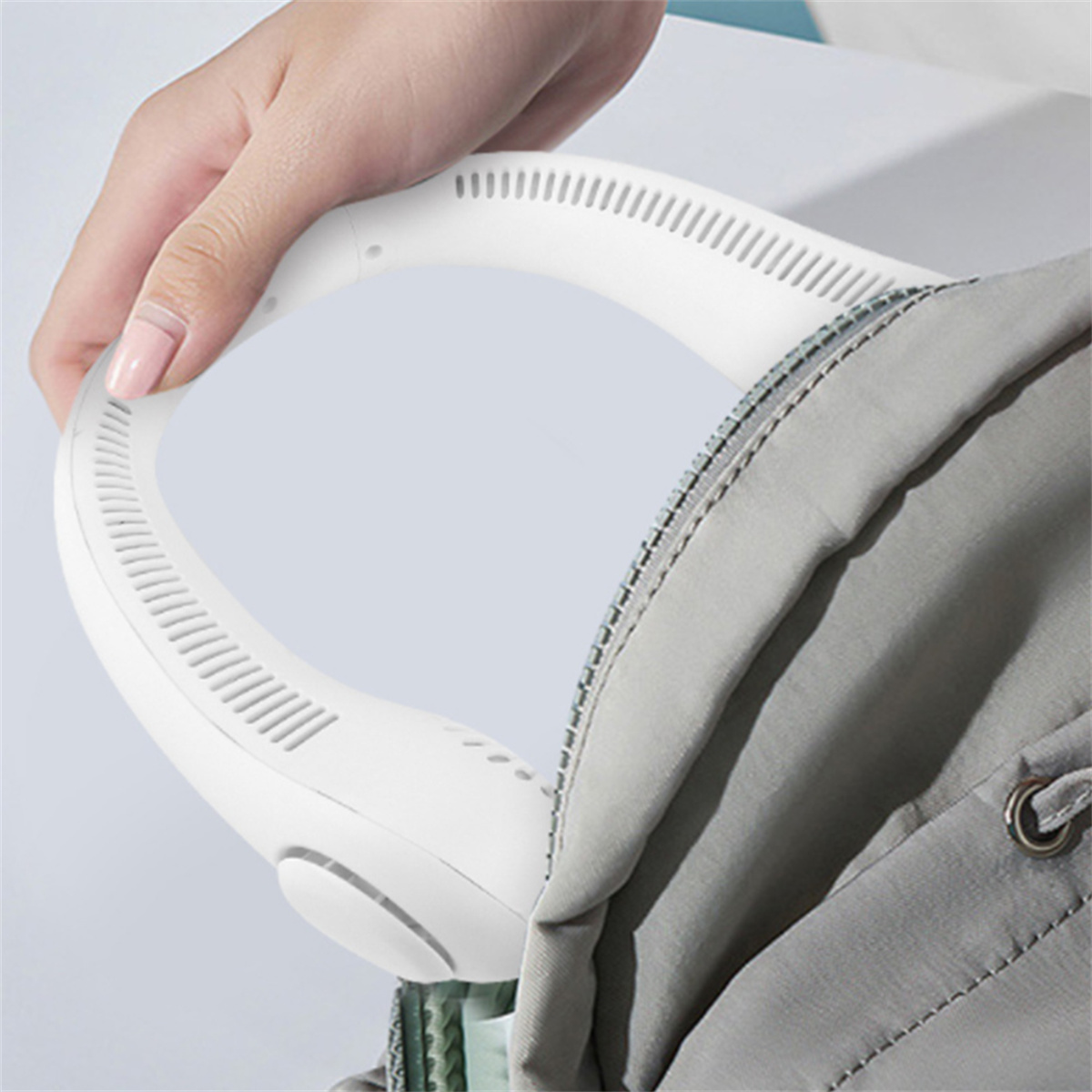 Die Hand einer Person hält einen weißen Nackenfächer. Der Ventilator liegt um den Hals und in der Tasche.