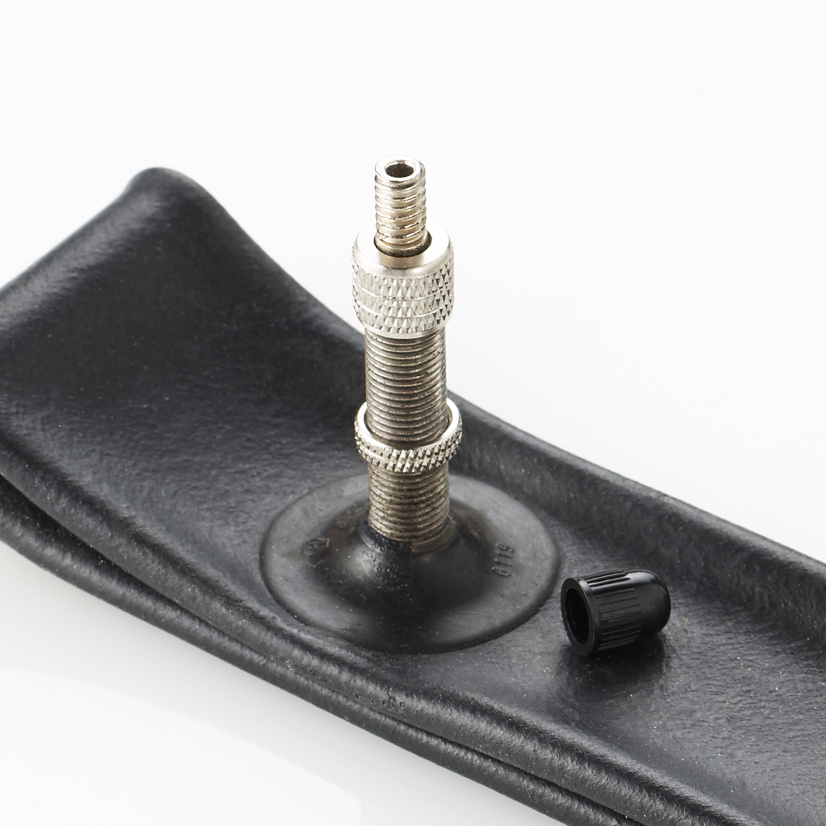 Trzpień zaworu dętki z czarną nasadką. Dętka jest czarna, na białej powierzchni.